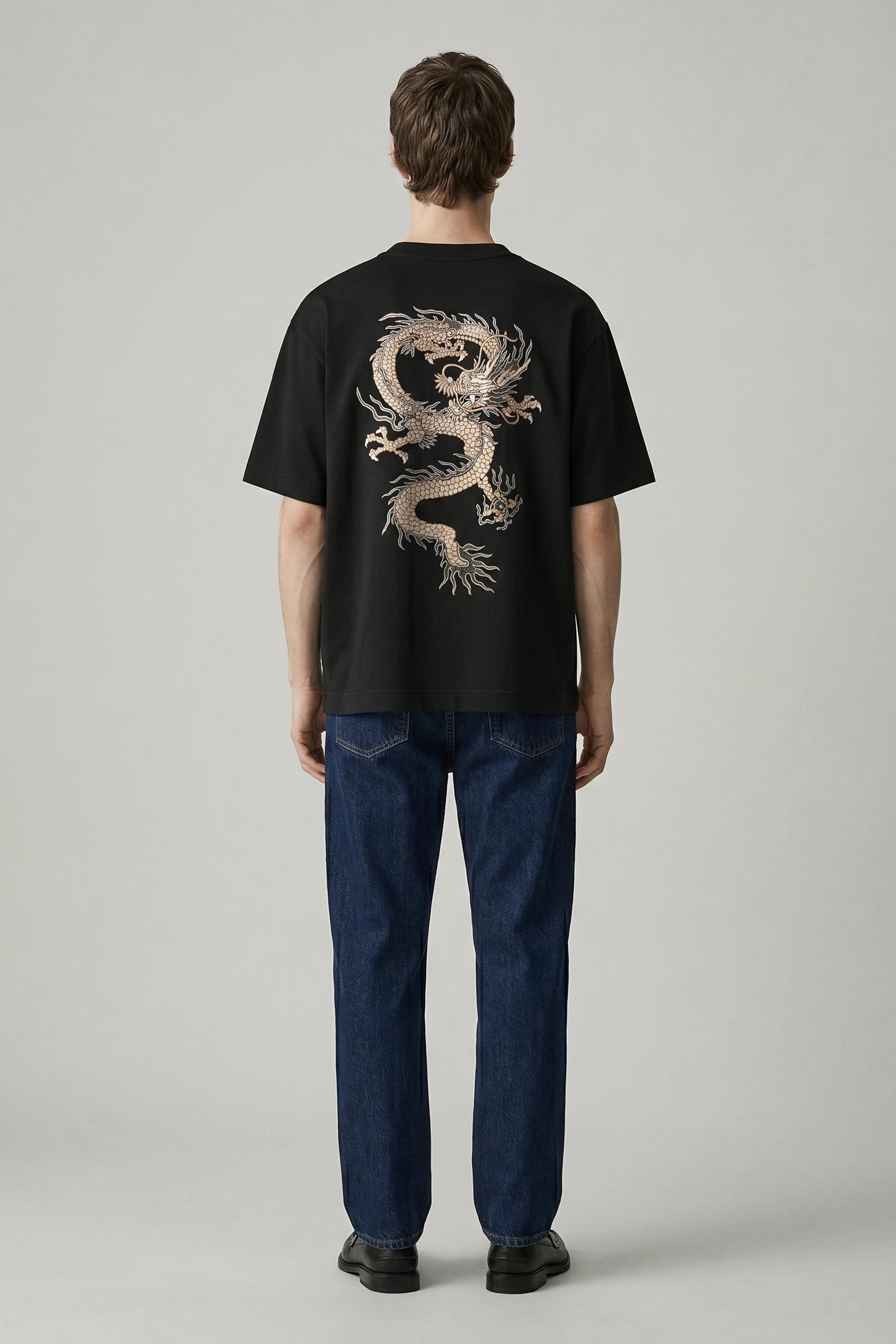 Person wearing a black t-shirt with a dragon design on the back, standing against a plain background.