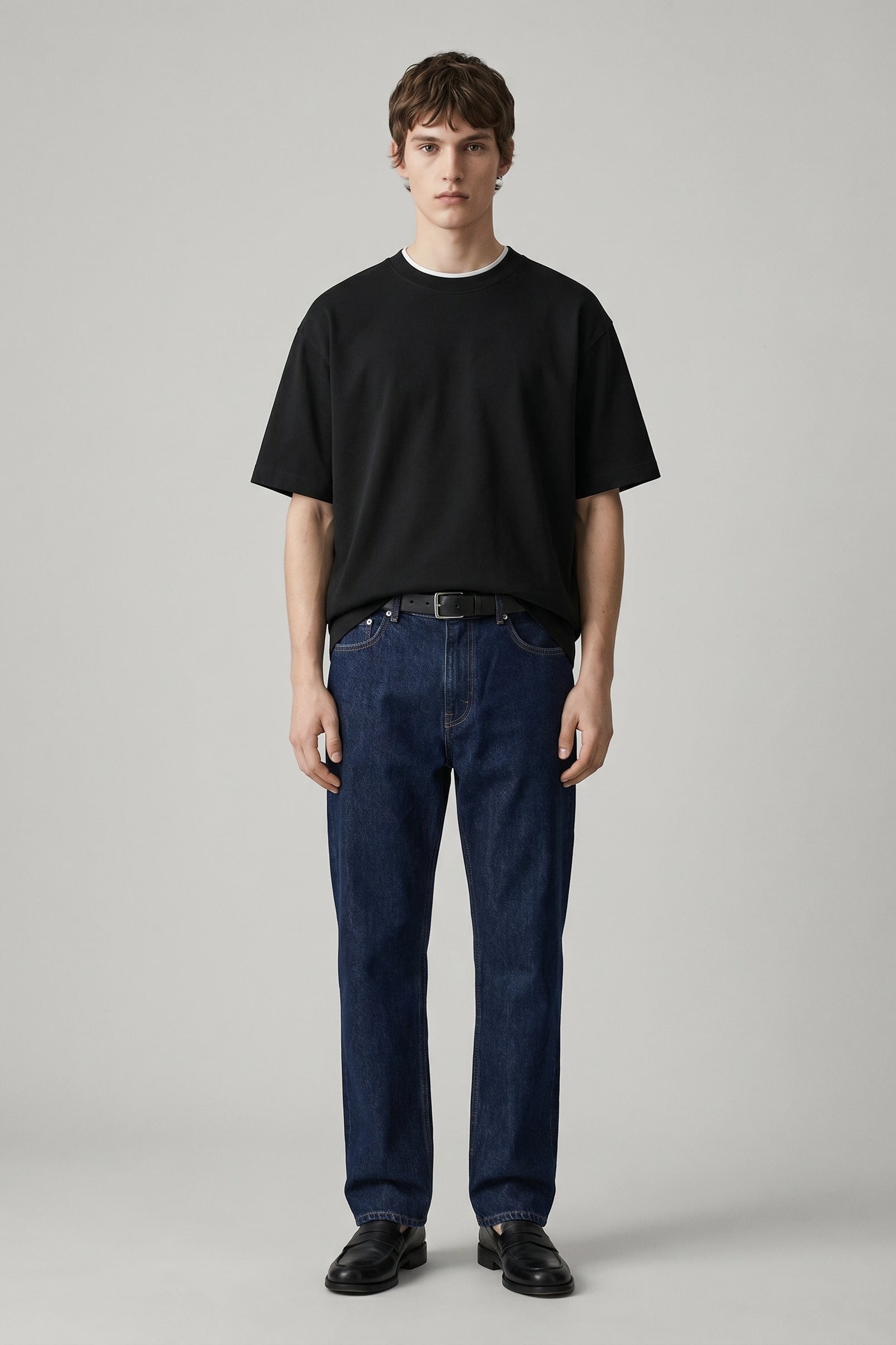 Man wearing a black t-shirt and blue jeans on a gray background