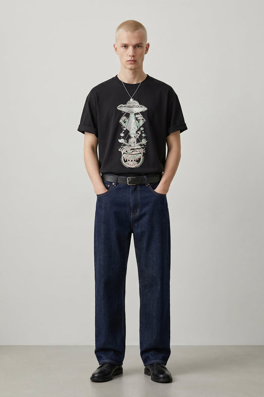 Man wearing a black t-shirt with a graphic design and dark jeans against a plain background