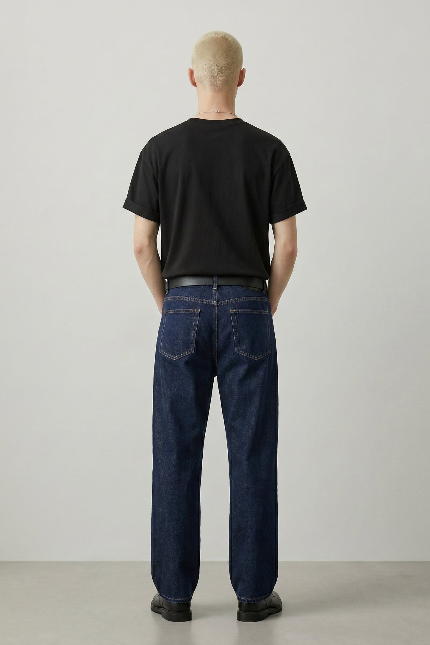 Person wearing a black t-shirt and dark blue jeans standing against a plain white background