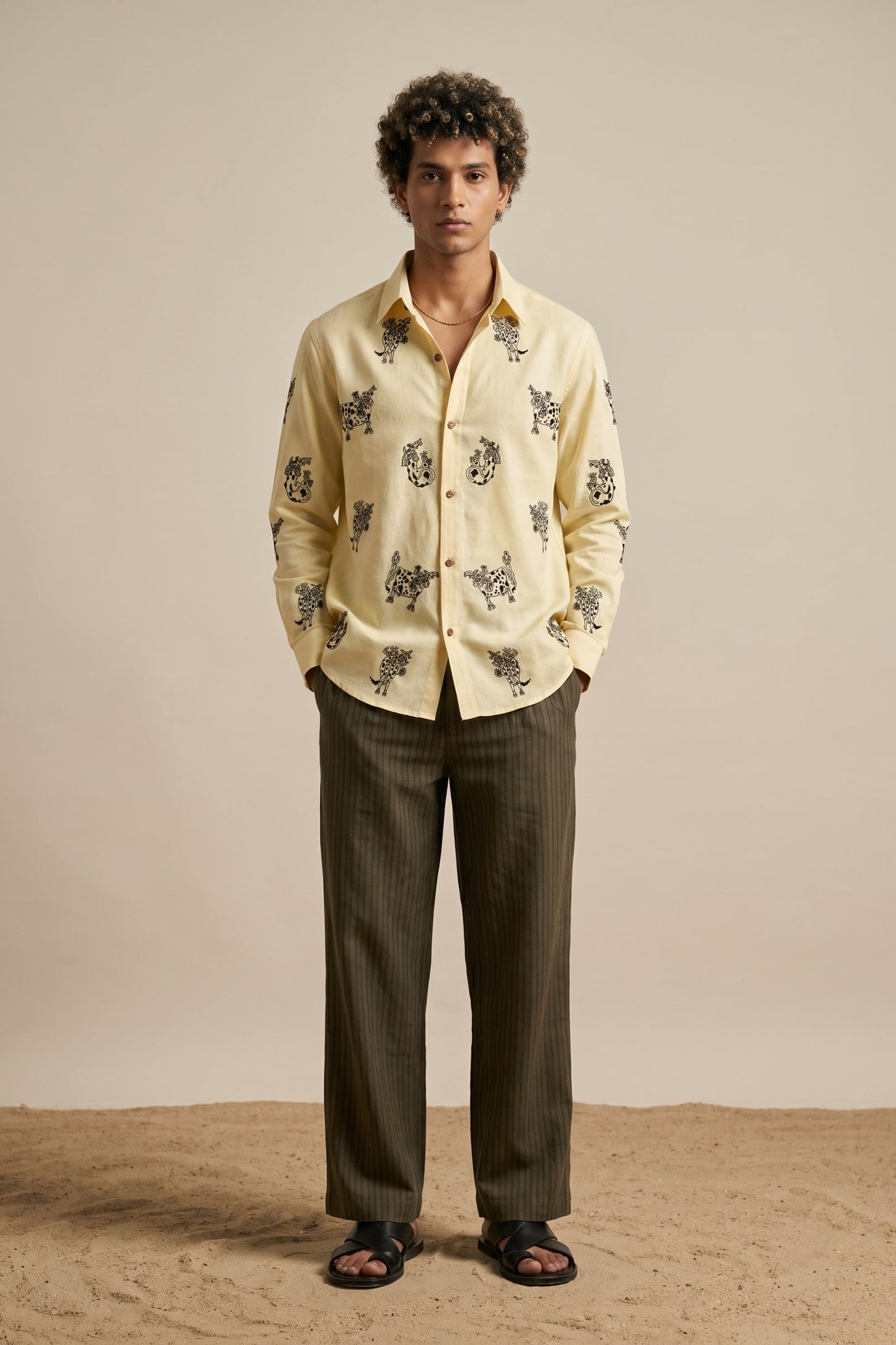 Man wearing a light-colored shirt with a pattern and dark pants on a beige background