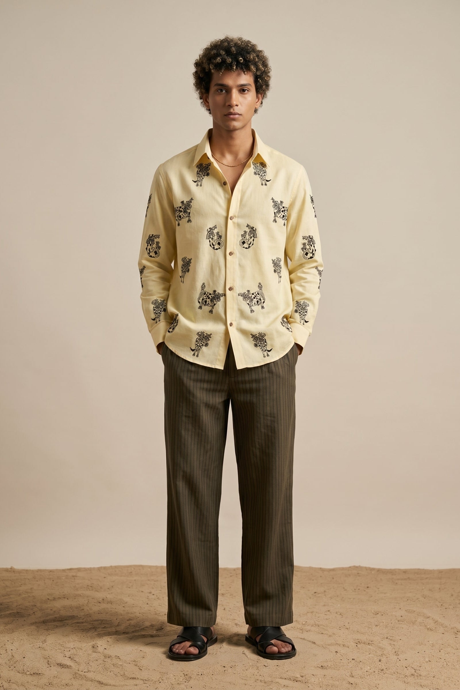 Man wearing a light-colored shirt with a pattern and dark pants on a beige background