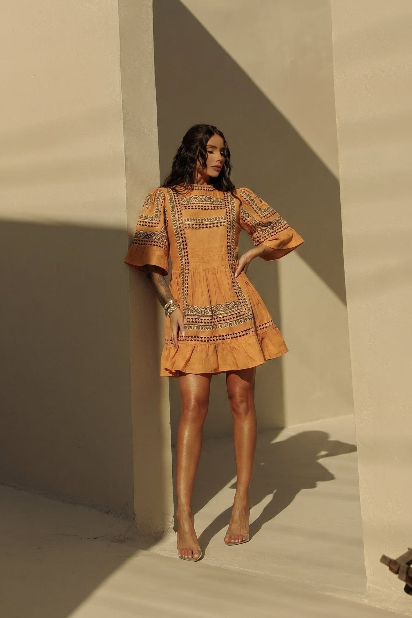 Woman wearing a mustard yellow dress with intricate patterns against a neutral wall.