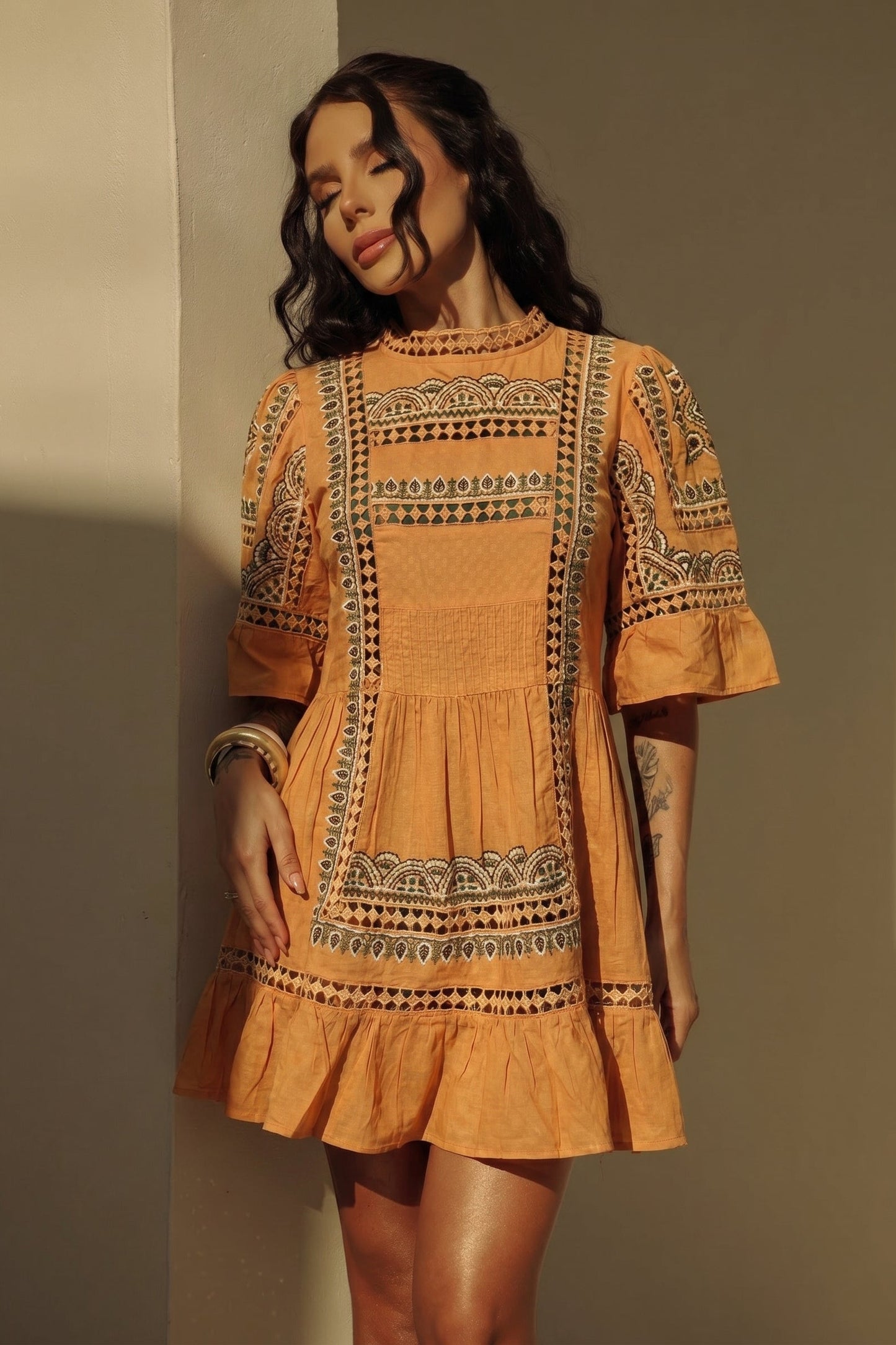 Woman wearing an orange  dress with intricate patterns against a neutral background