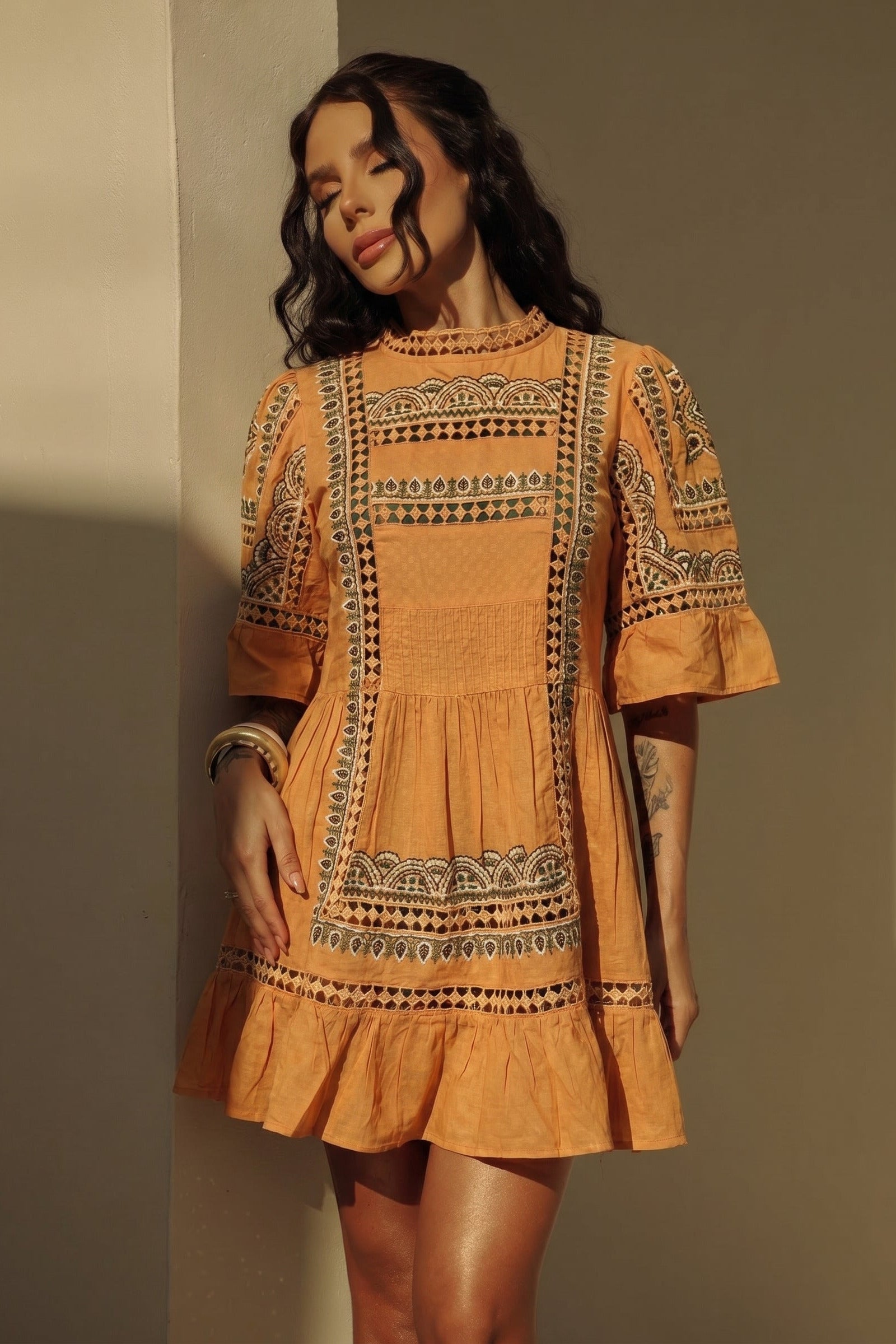 Woman wearing an orange  dress with intricate patterns against a neutral background