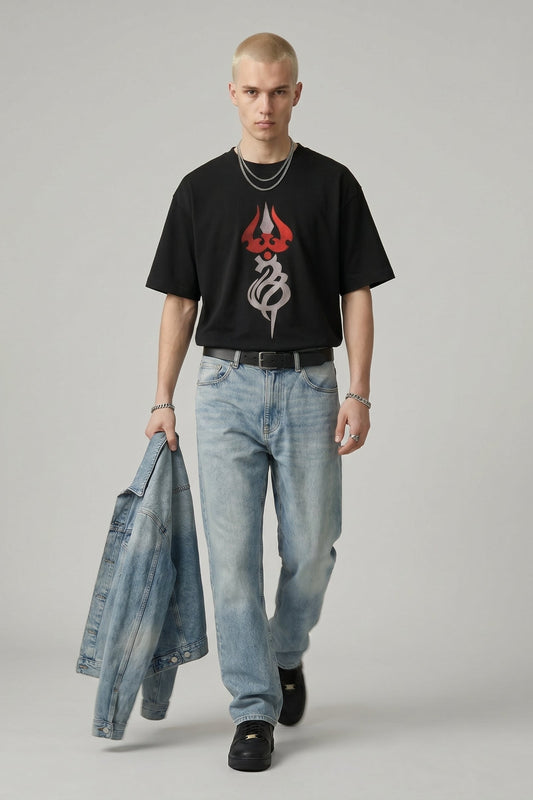 Man wearing a black t-shirt with a logo and light blue jeans, holding a denim jacket.