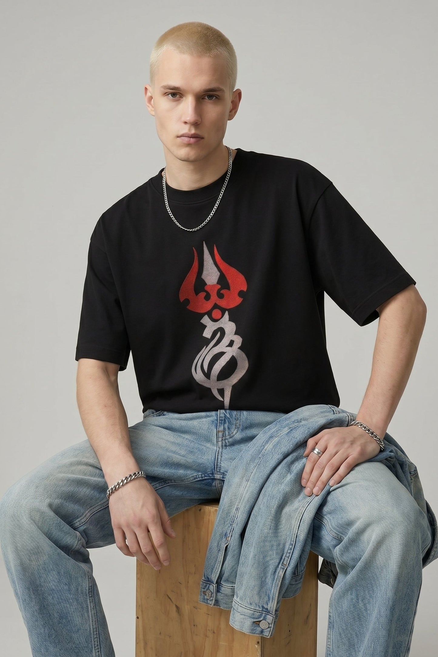 Person wearing a black t-shirt with a graphic design sitting on a wooden stool against a plain background