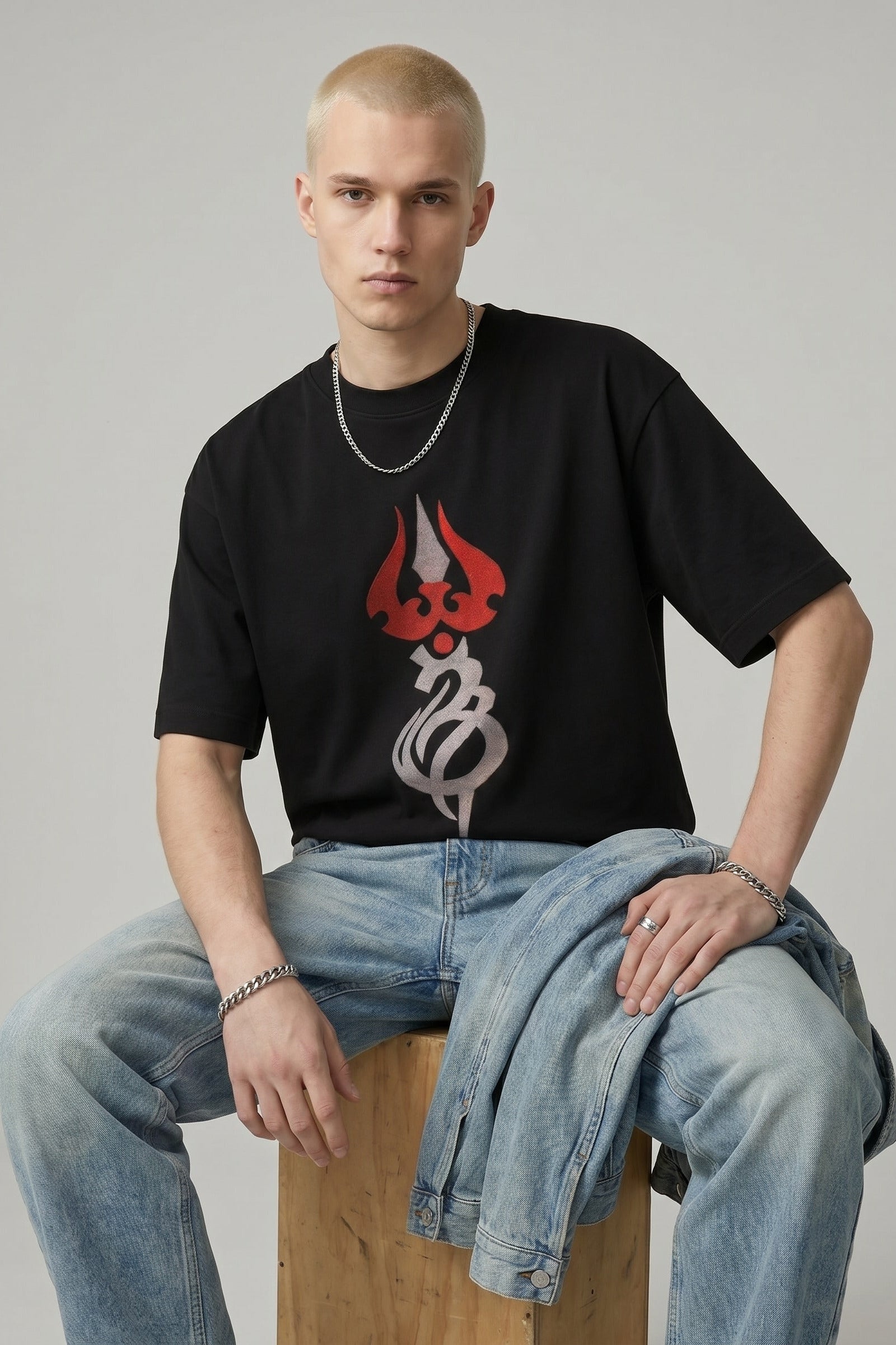 Person wearing a black t-shirt with a graphic design sitting on a wooden stool against a plain background