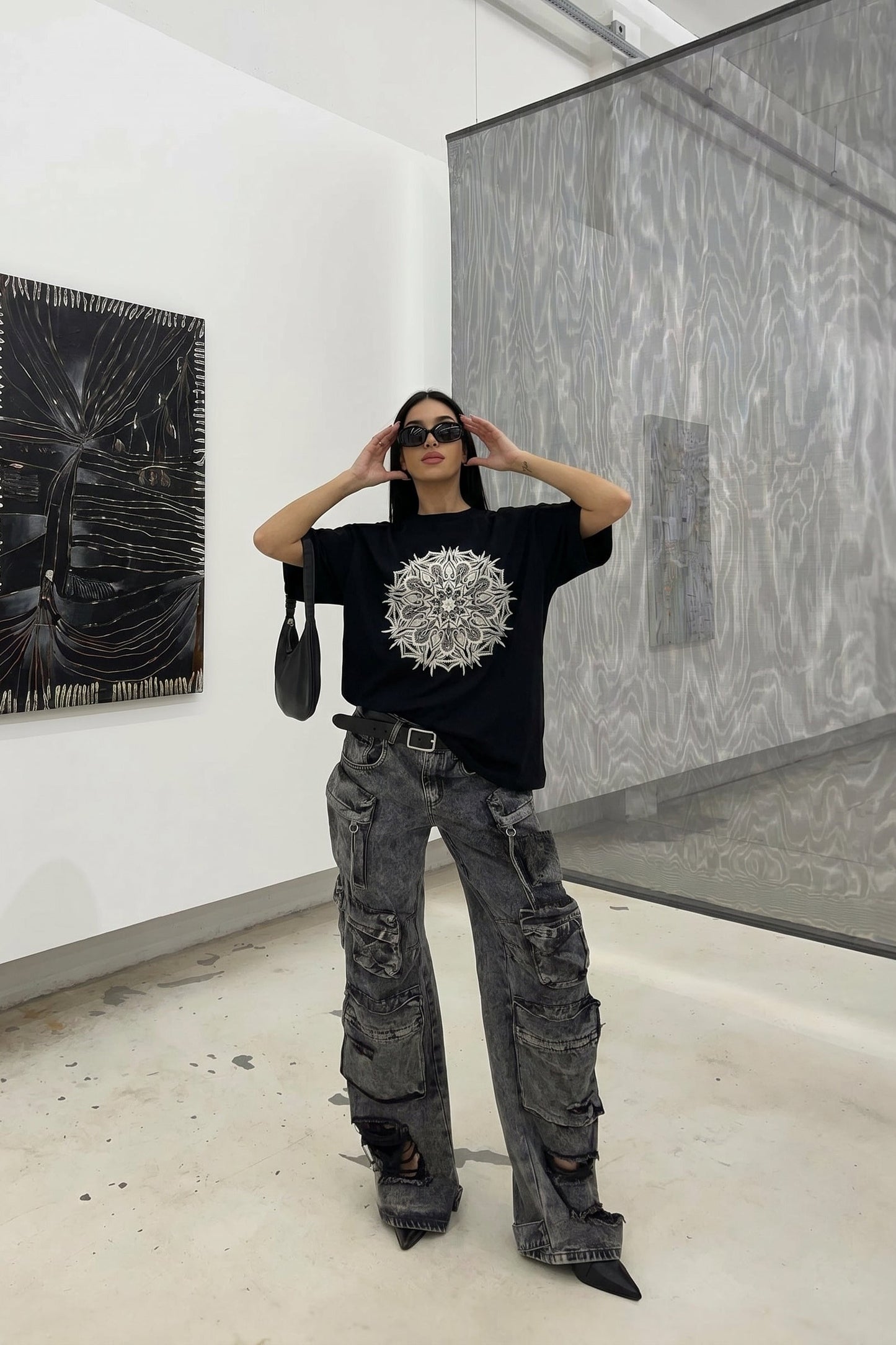 Person wearing a black t-shirt with a white design and gray pants in an art gallery.
