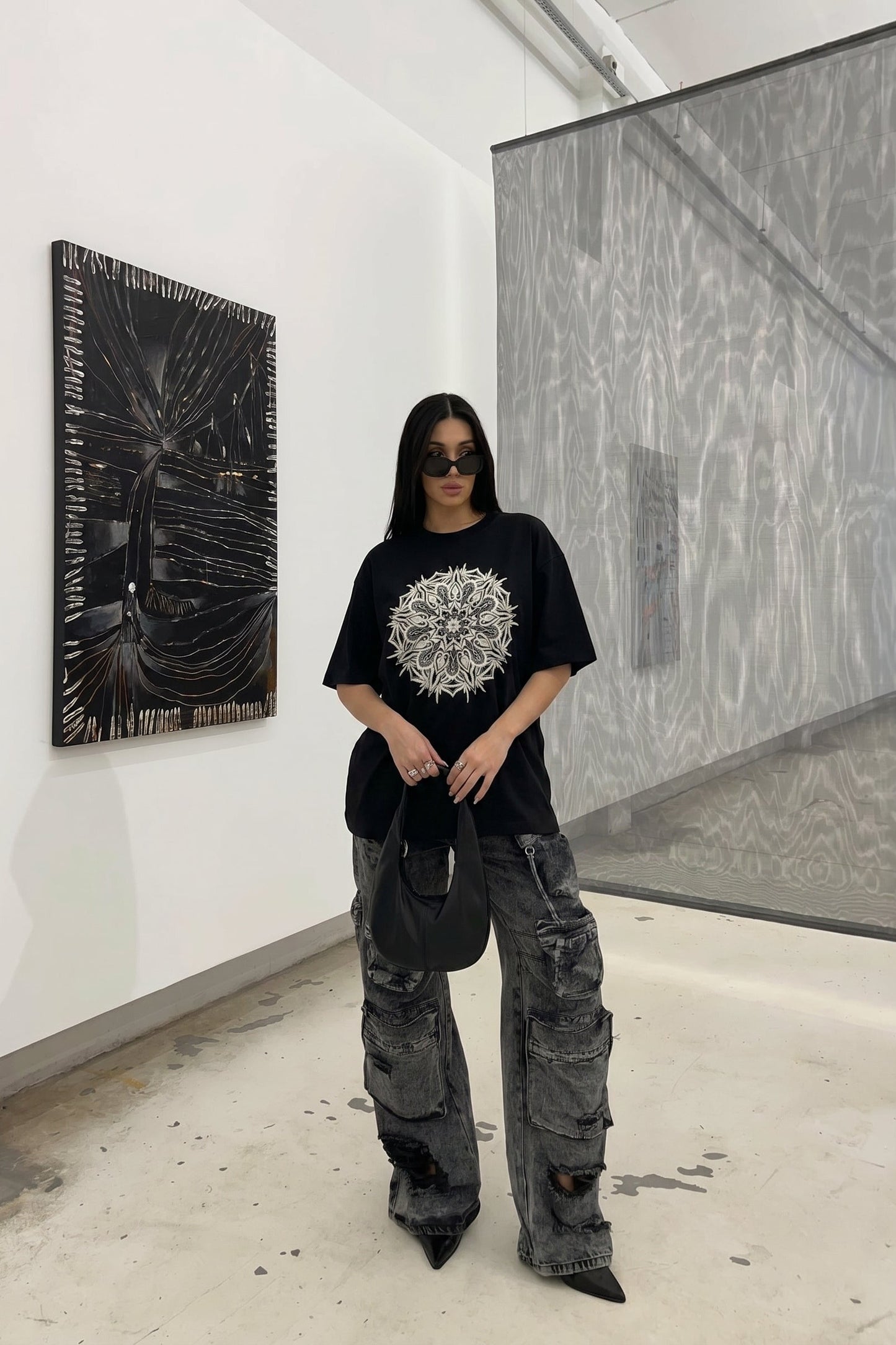 Person wearing a black t-shirt with a white design and gray cargo pants in an art gallery.