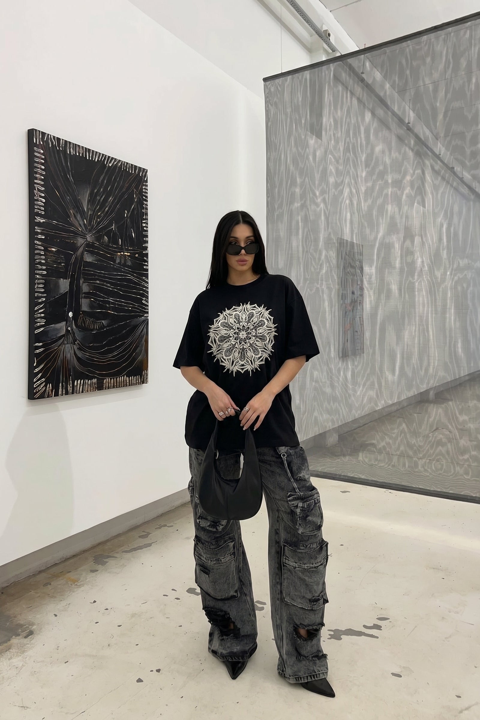 Person wearing a black t-shirt with a white design and gray cargo pants in an art gallery.