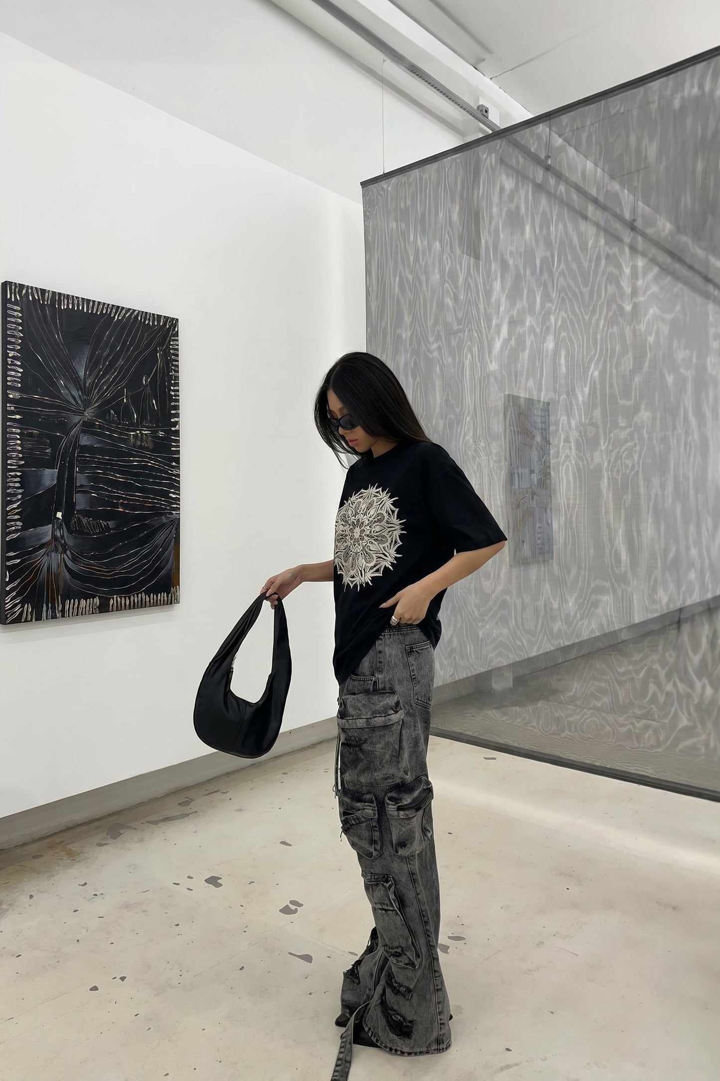 Person in an art gallery holding a black handbag, wearing a black t-shirt with a white design and gray pants.