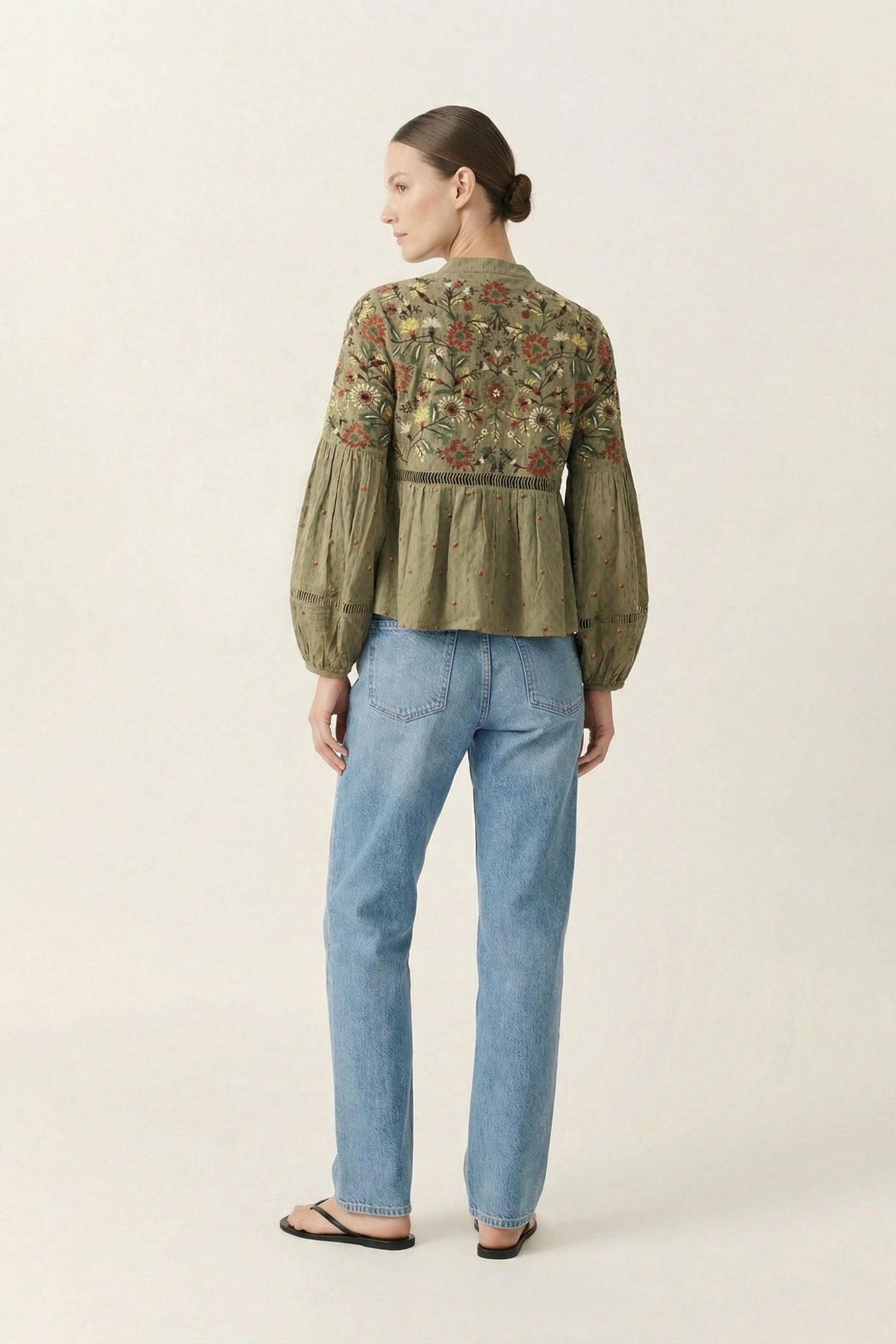 Woman wearing a green embroidered blouse and blue jeans on a white background