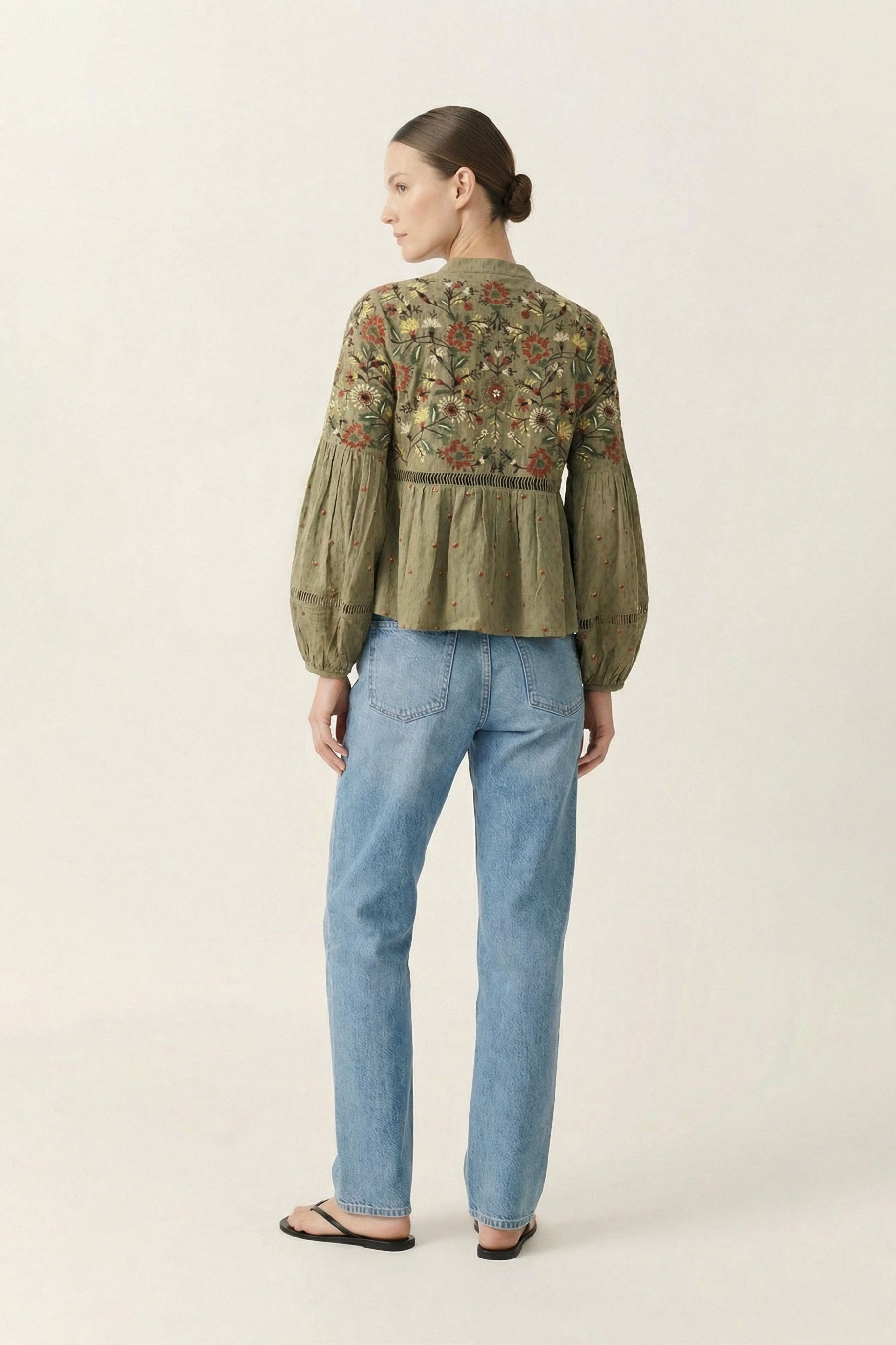 Woman wearing a green embroidered blouse and blue jeans on a white background