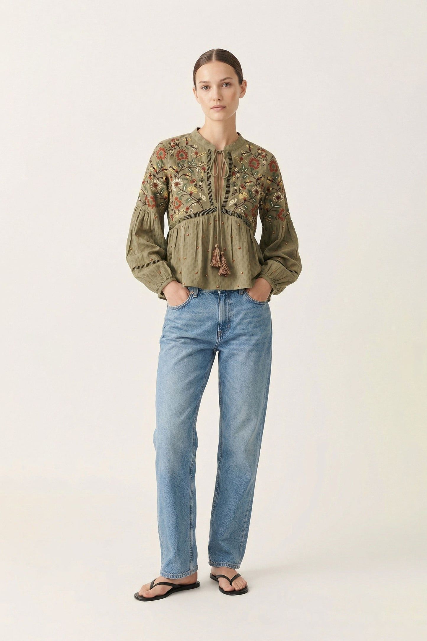 Woman wearing a patterned blouse and blue jeans on a white background