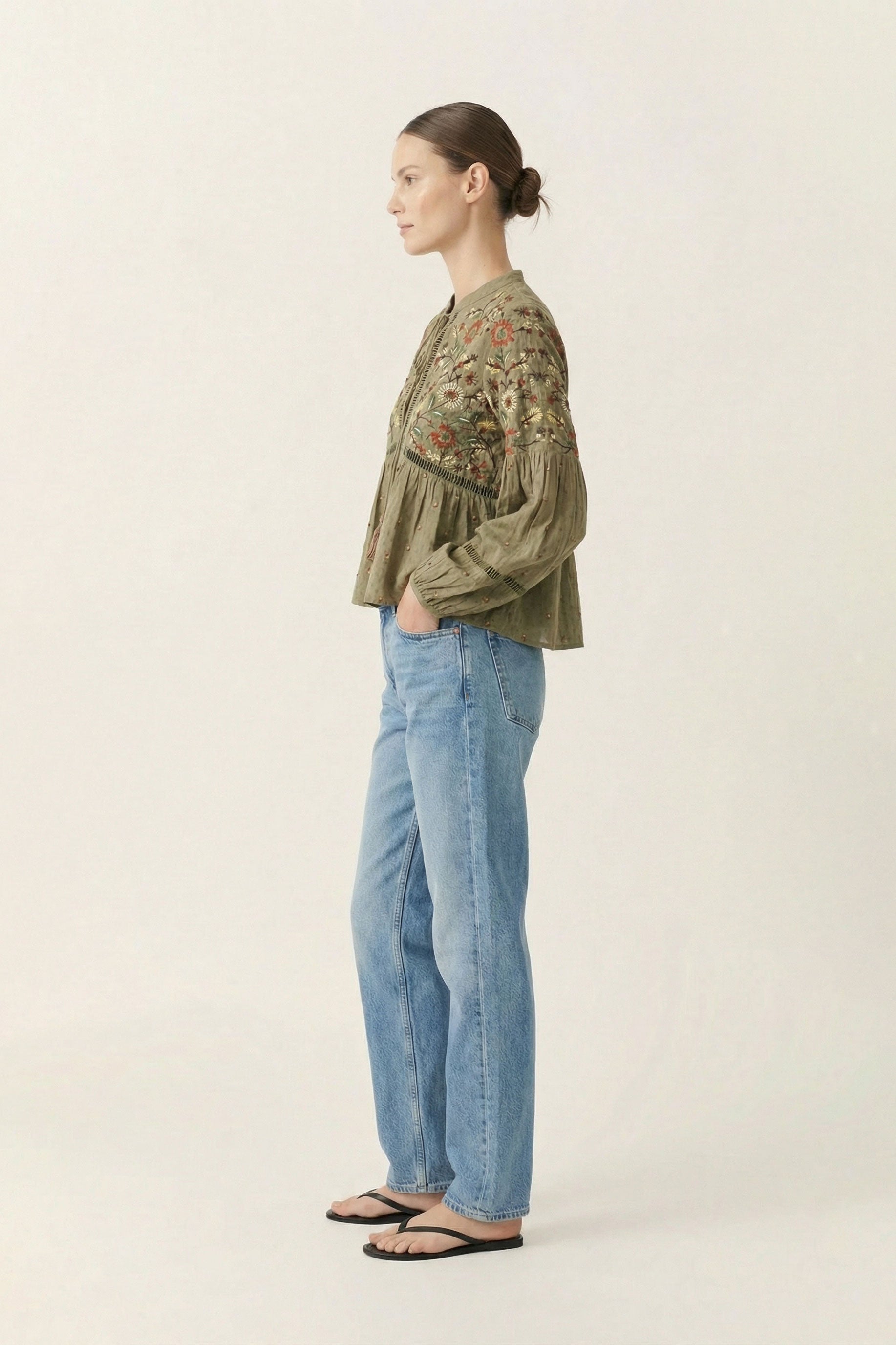 Woman wearing a green embroidered blouse and blue jeans on a white background