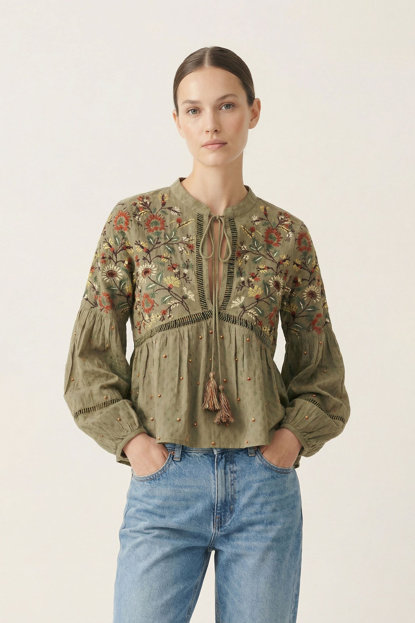 Woman wearing a green embroidered blouse and blue jeans on a white background