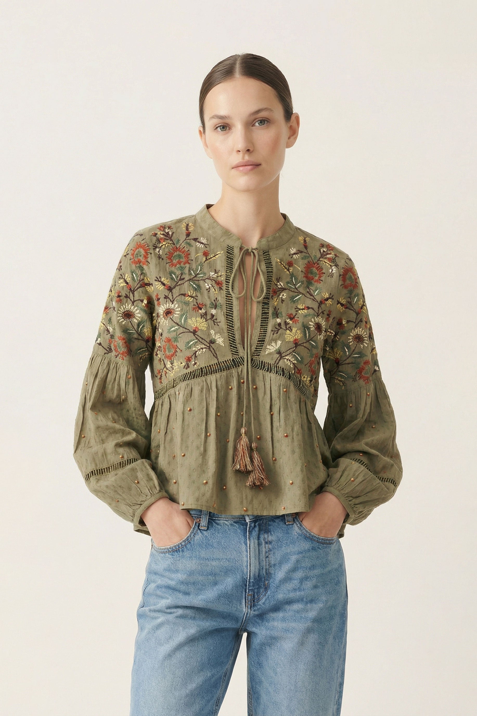 Woman wearing a green embroidered blouse and blue jeans on a white background