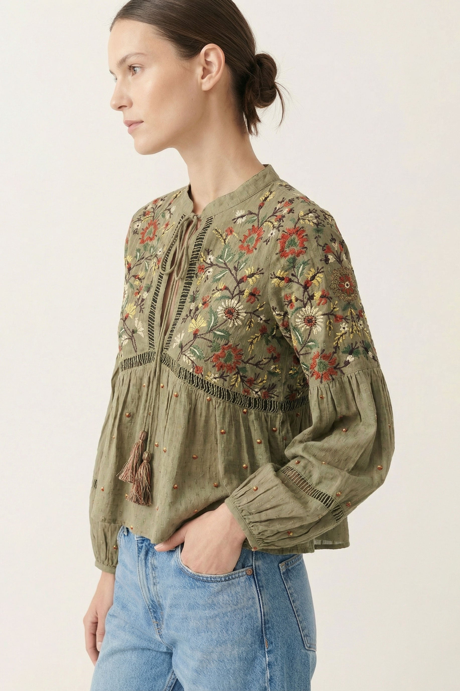 Woman wearing a green embroidered blouse with blue jeans on a white background