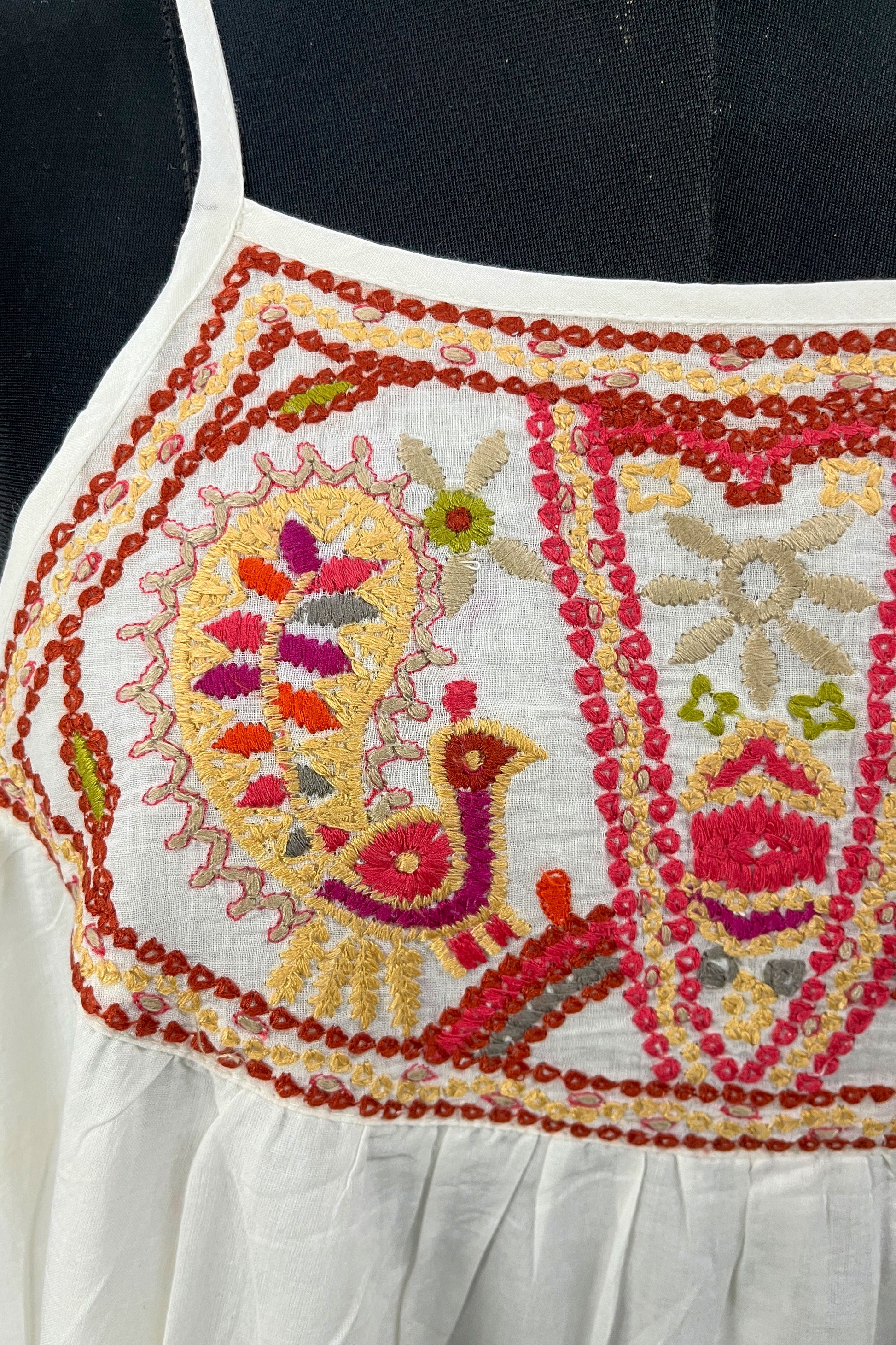 Close-up of a white garment with intricate multicolored embroidery on a black background