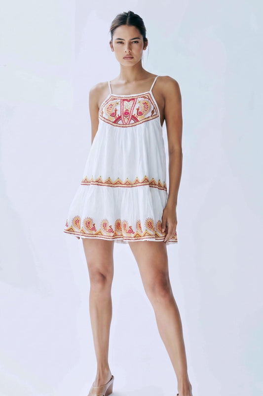 Woman wearing a white dress with floral embroidery on a plain background
