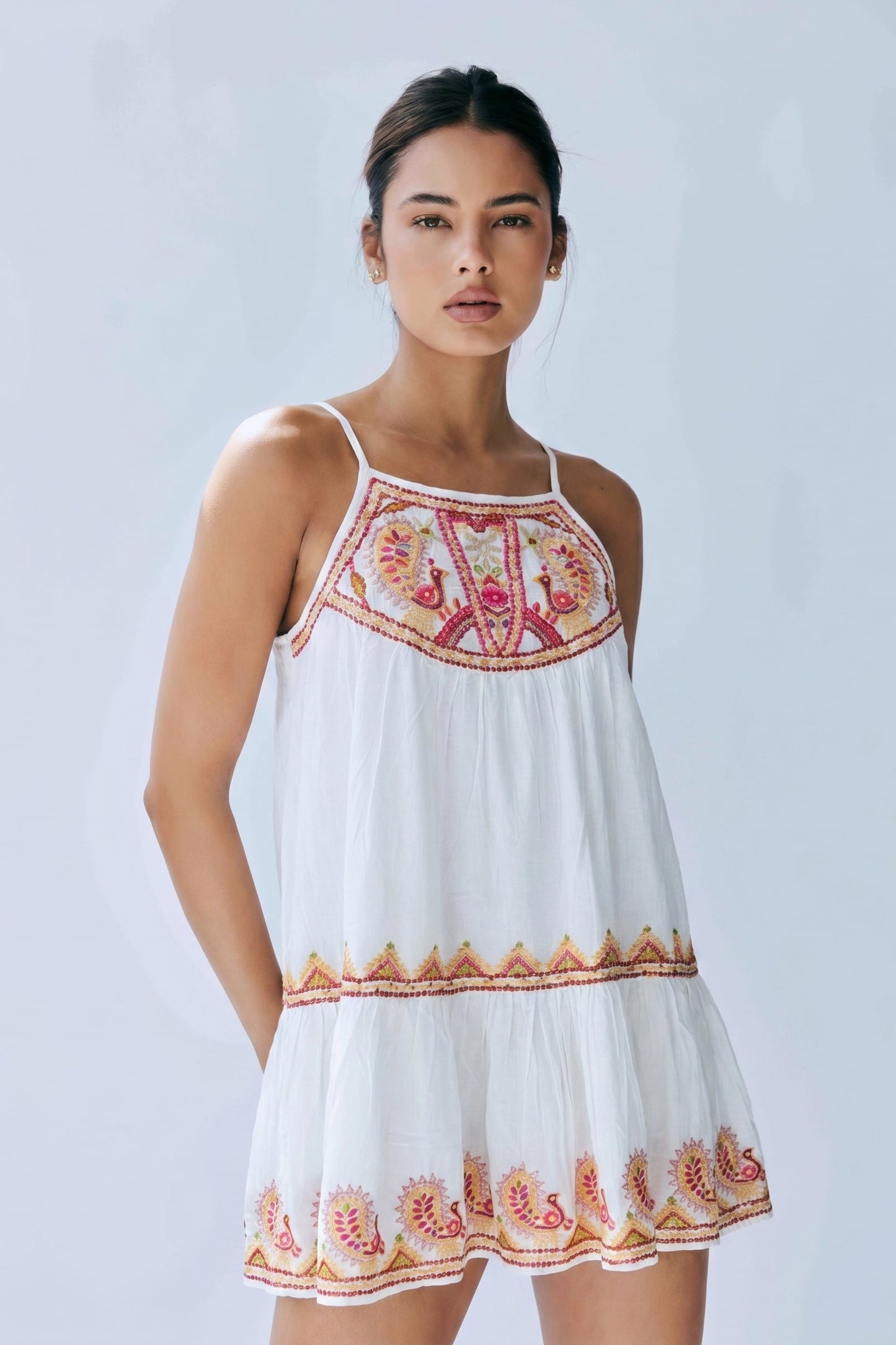 Woman wearing a white dress with floral embroidery on a light gray background