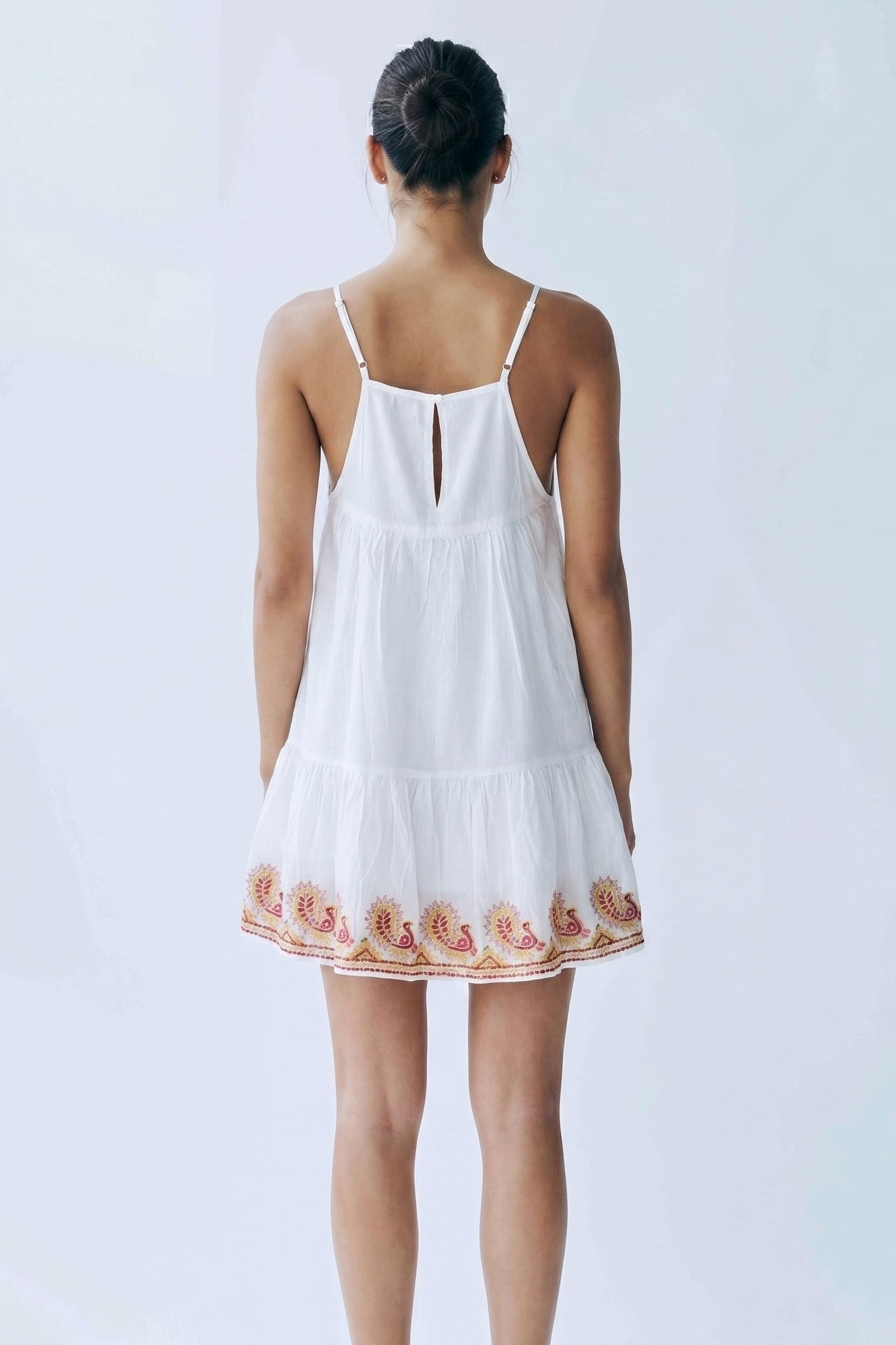Woman wearing a white dress with floral embroidery on a plain background