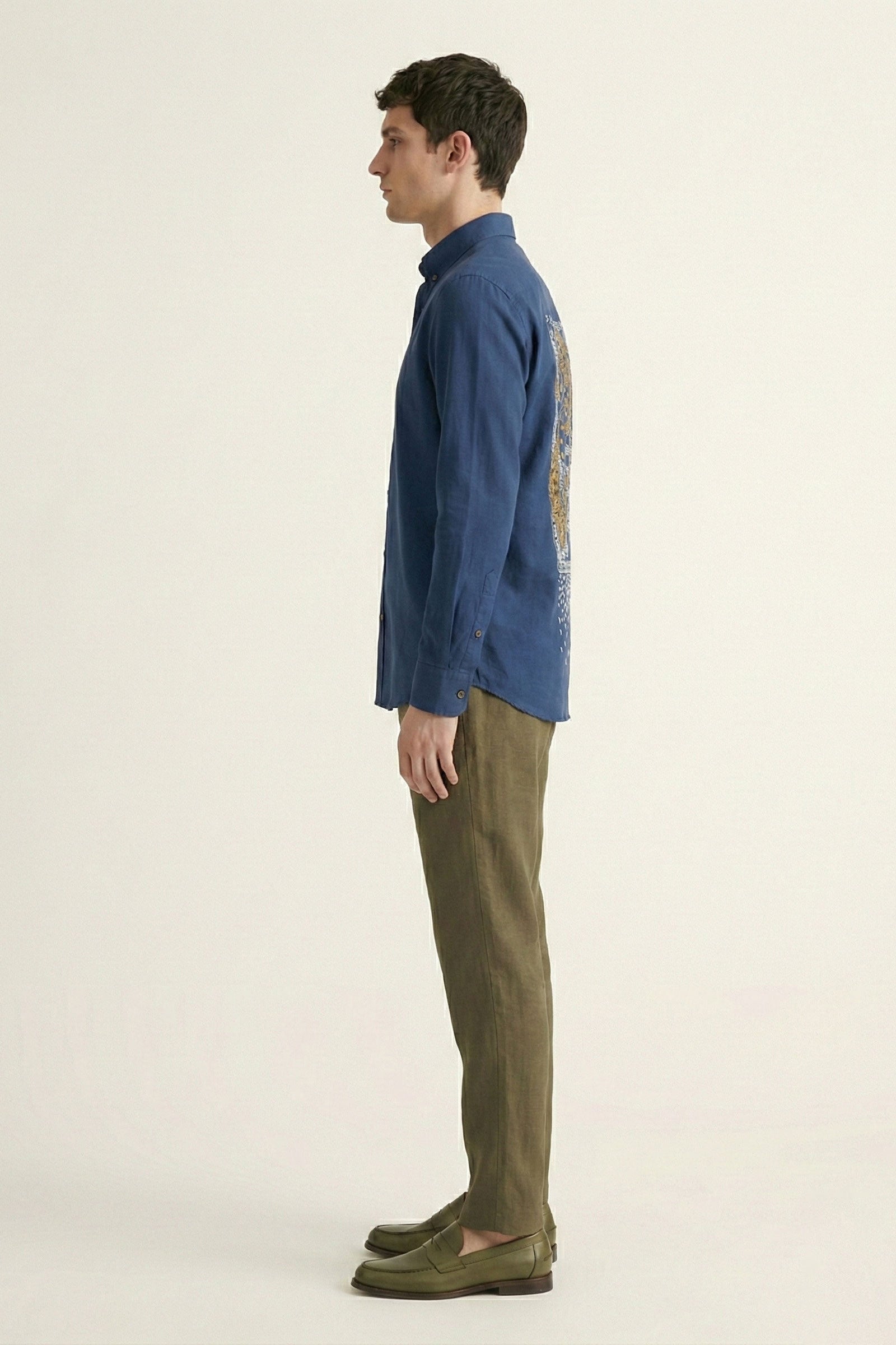 Man wearing a blue shirt with a patterned sleeve and green pants on a beige background