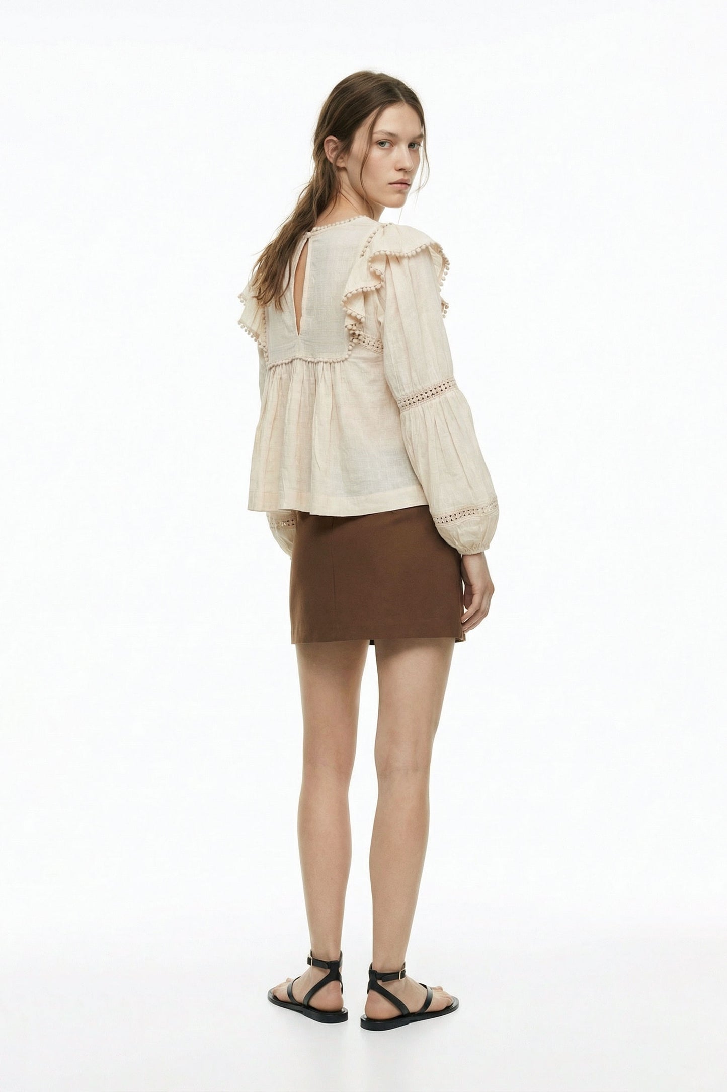 Woman wearing a beige blouse with ruffled sleeves and a brown skirt on a white background