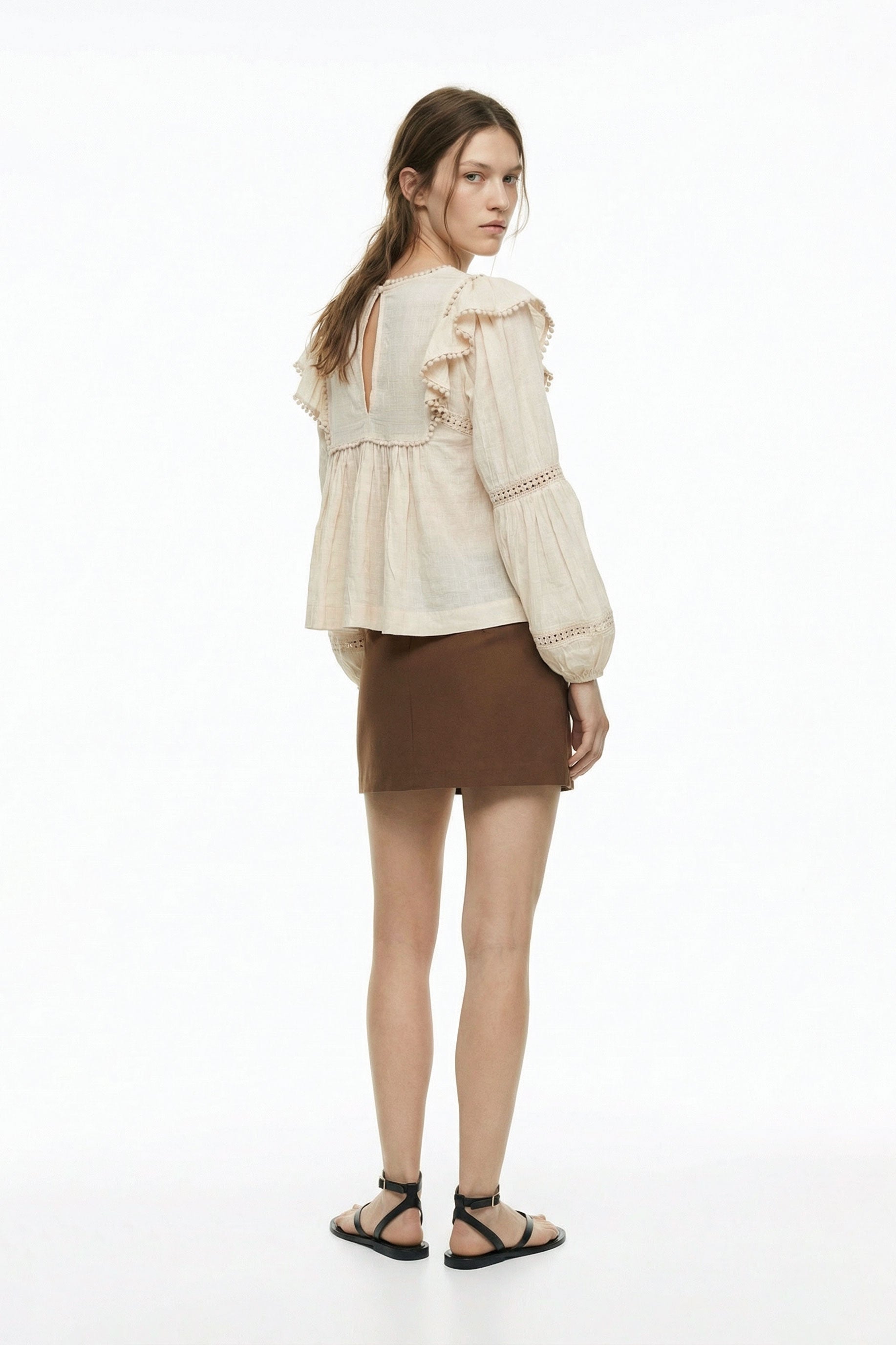 Woman wearing a beige blouse with ruffled sleeves and a brown skirt on a white background