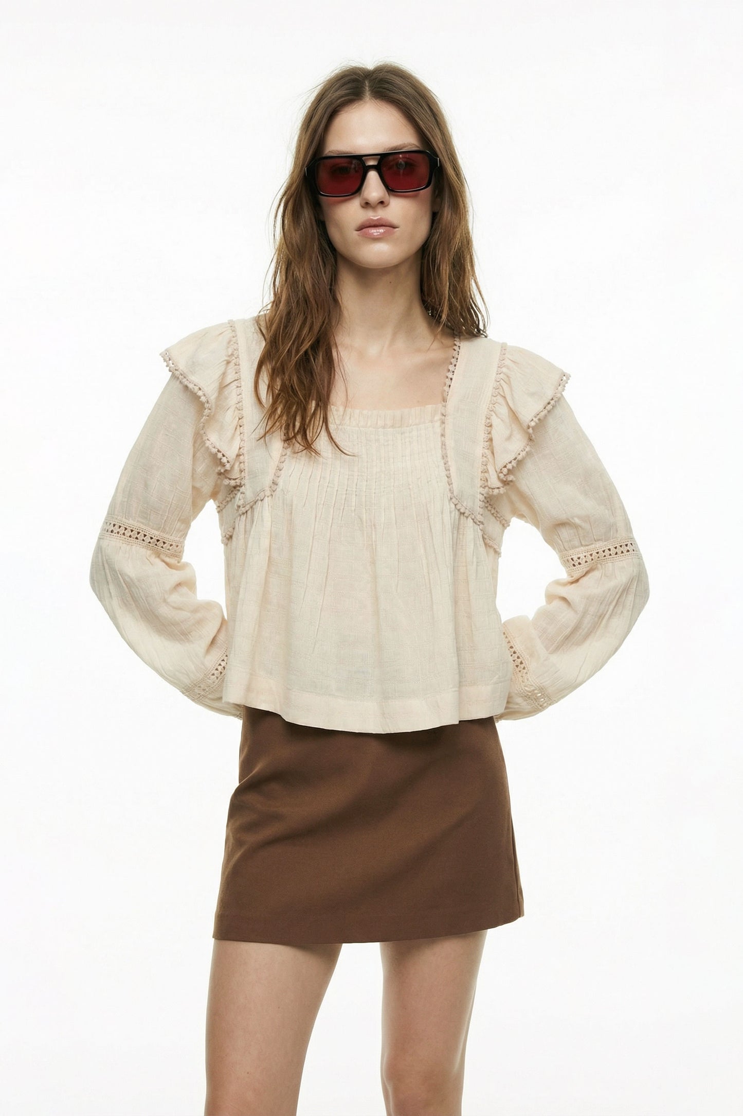 Woman wearing a beige blouse with ruffled sleeves and a brown skirt on a white background