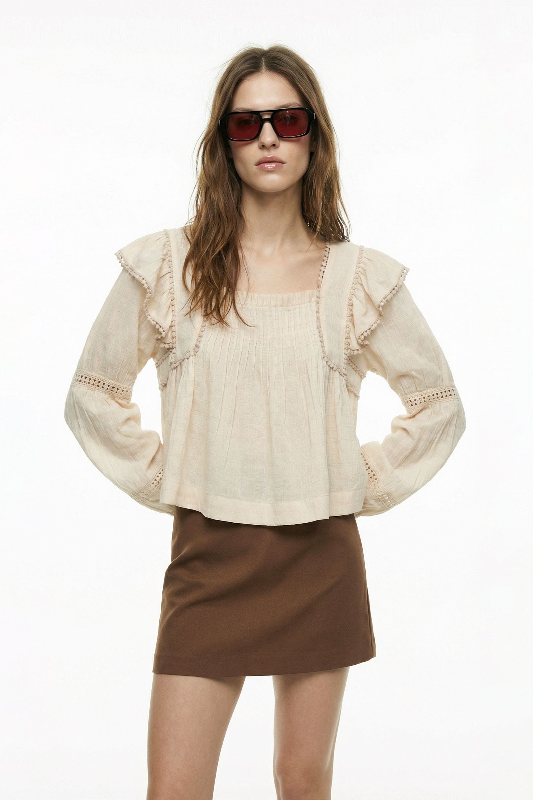 Woman wearing a beige blouse with ruffled sleeves and a brown skirt on a white background