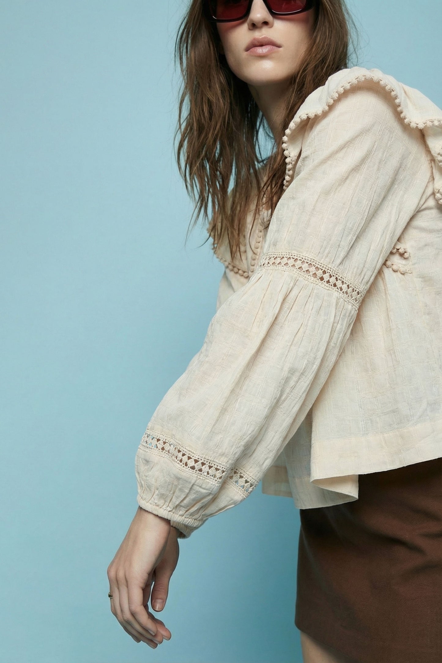 Woman wearing a beige blouse with lace details against a light blue background