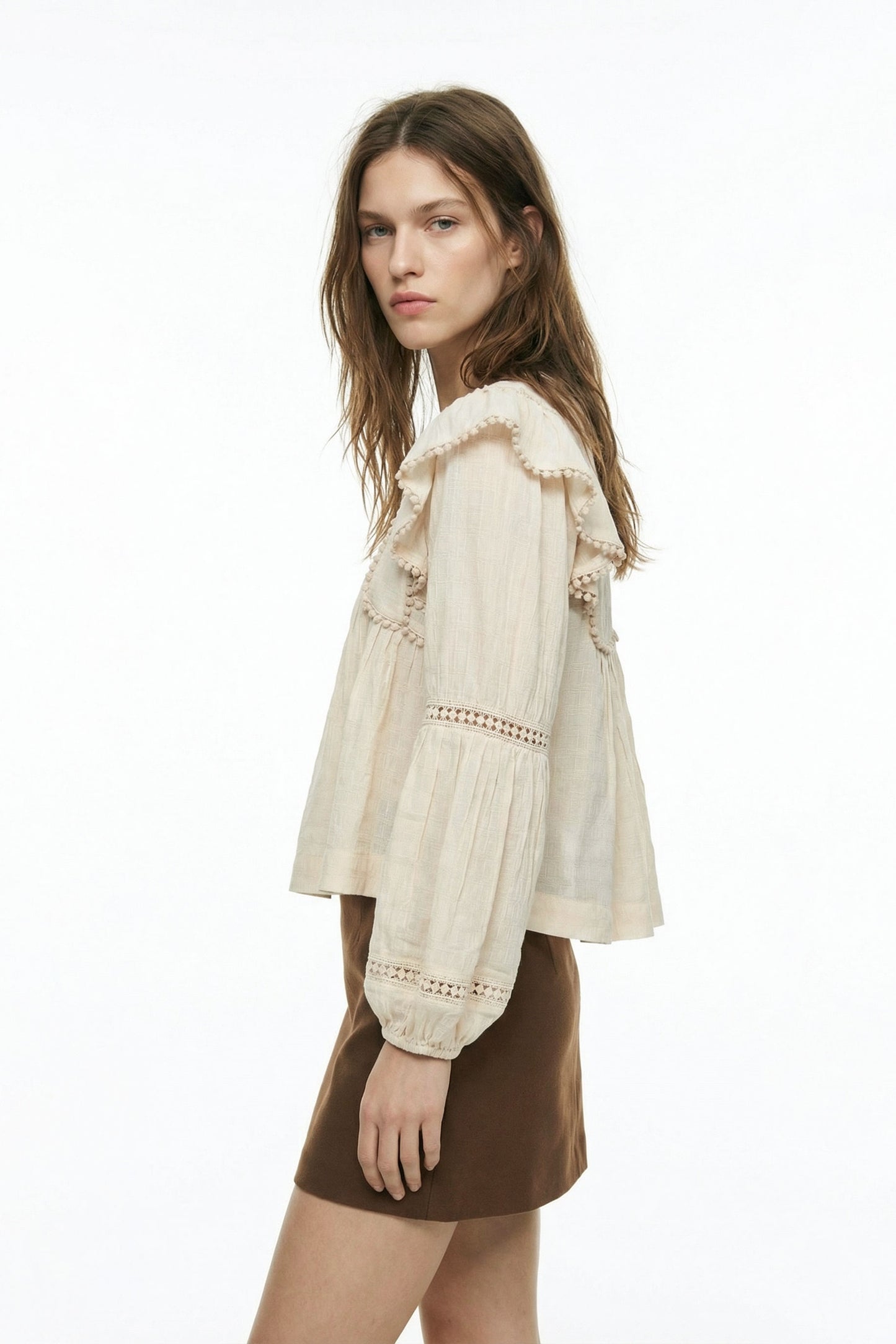 Woman wearing a beige blouse with lace details and a brown skirt on a white background