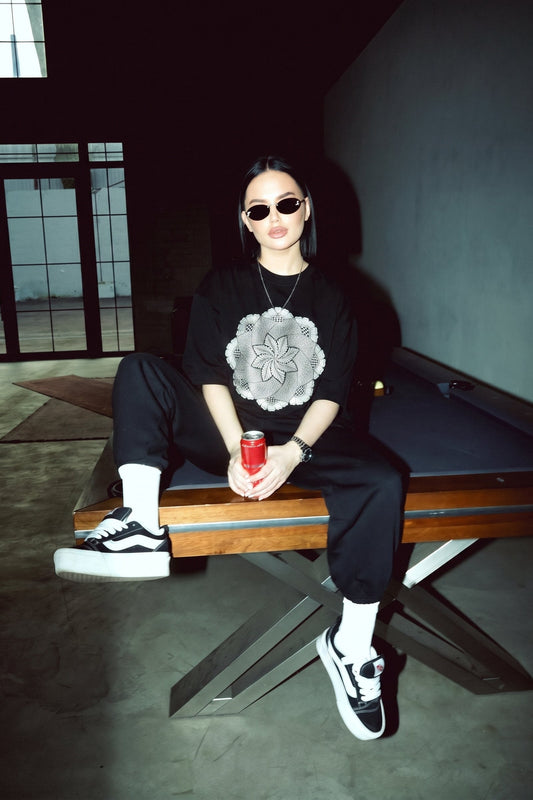 Person sitting on a pool table holding a red can, wearing a black outfit with a white flower design.