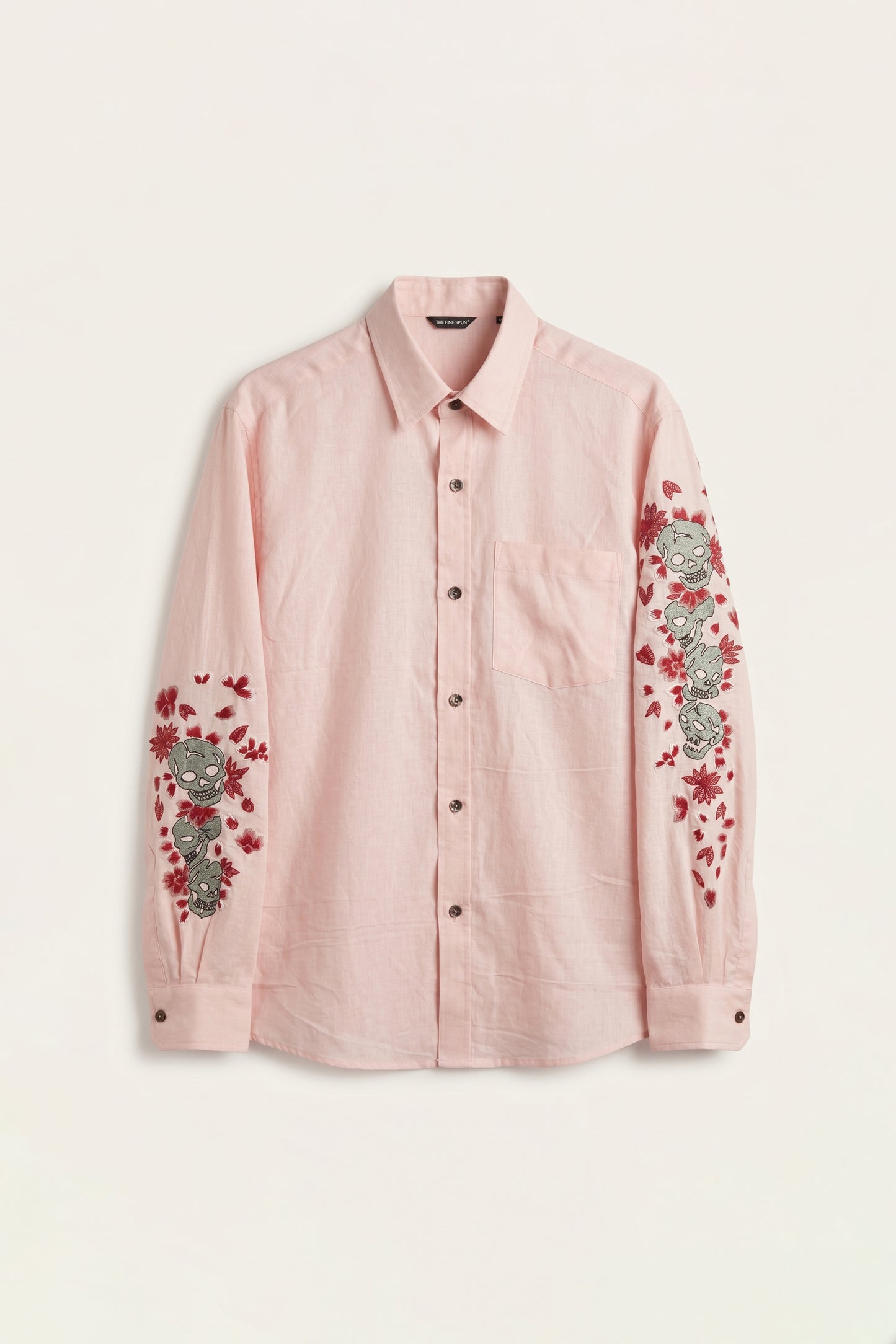 Pink shirt with floral and skull embroidery on a light beige background