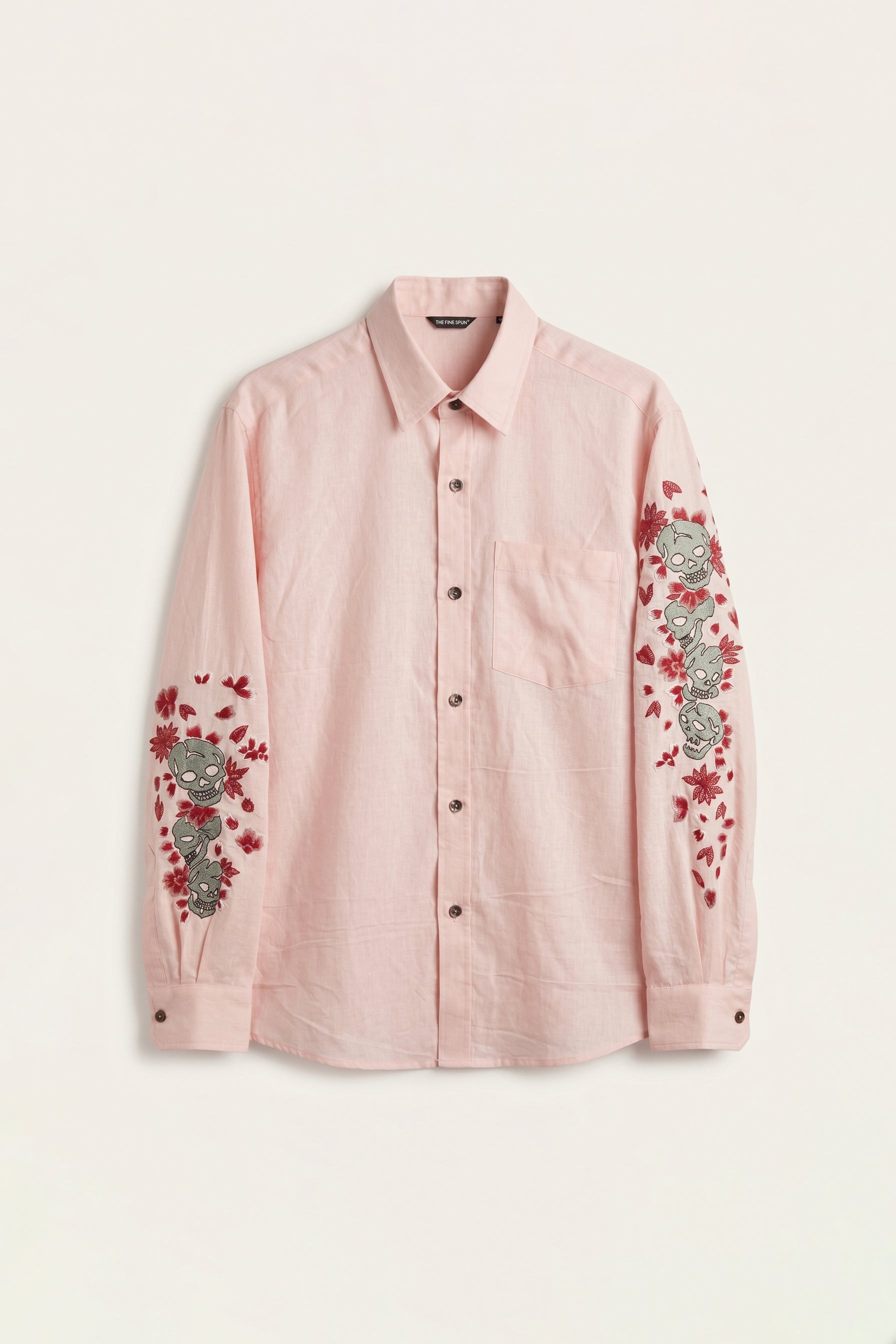 Pink shirt with floral and skull embroidery on a light beige background