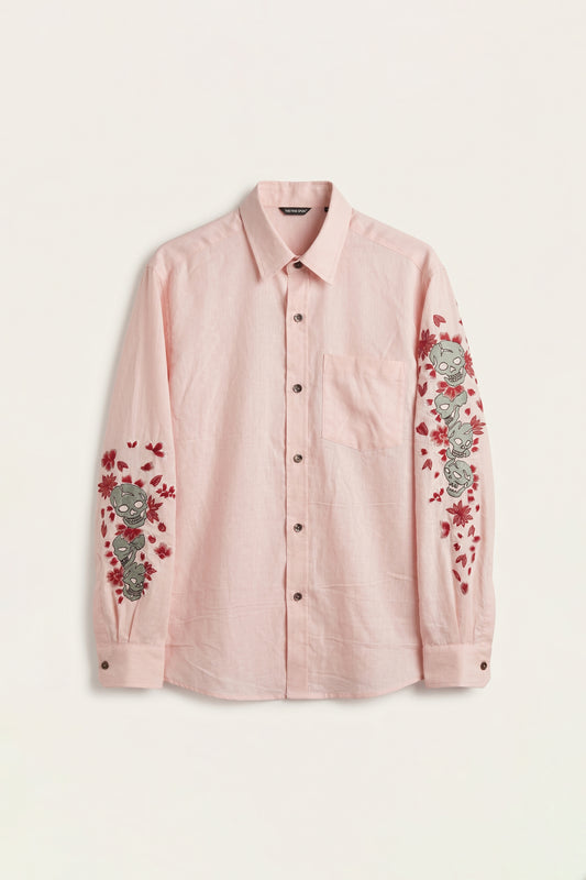 Pink shirt with floral and skull embroidery on a light beige background