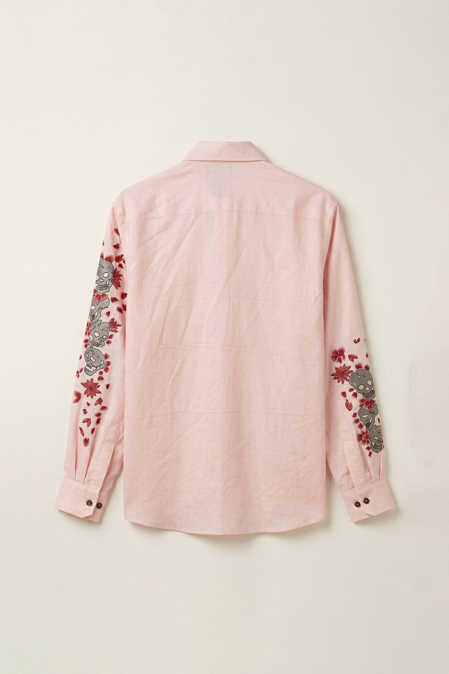 Pink shirt with floral and skull embroidery on a light beige background