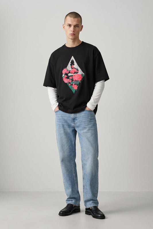 Man wearing a black t-shirt with a floral design and blue jeans on a gray background