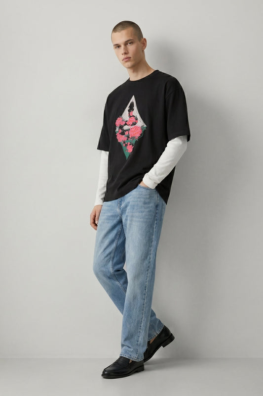 Person wearing a black t-shirt with a graphic design and light blue jeans on a plain background