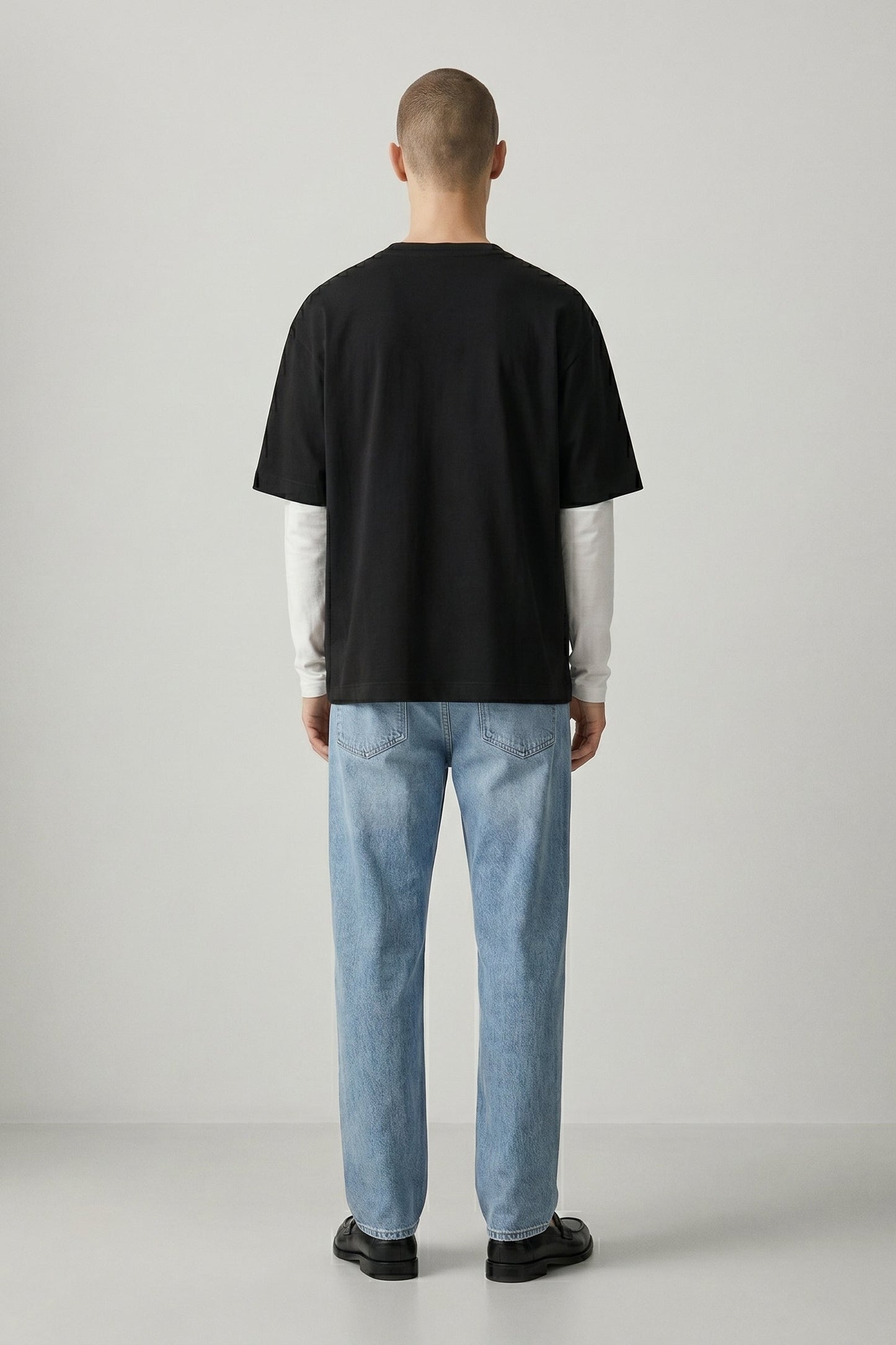 Person wearing a black t-shirt and light blue jeans standing against a plain background