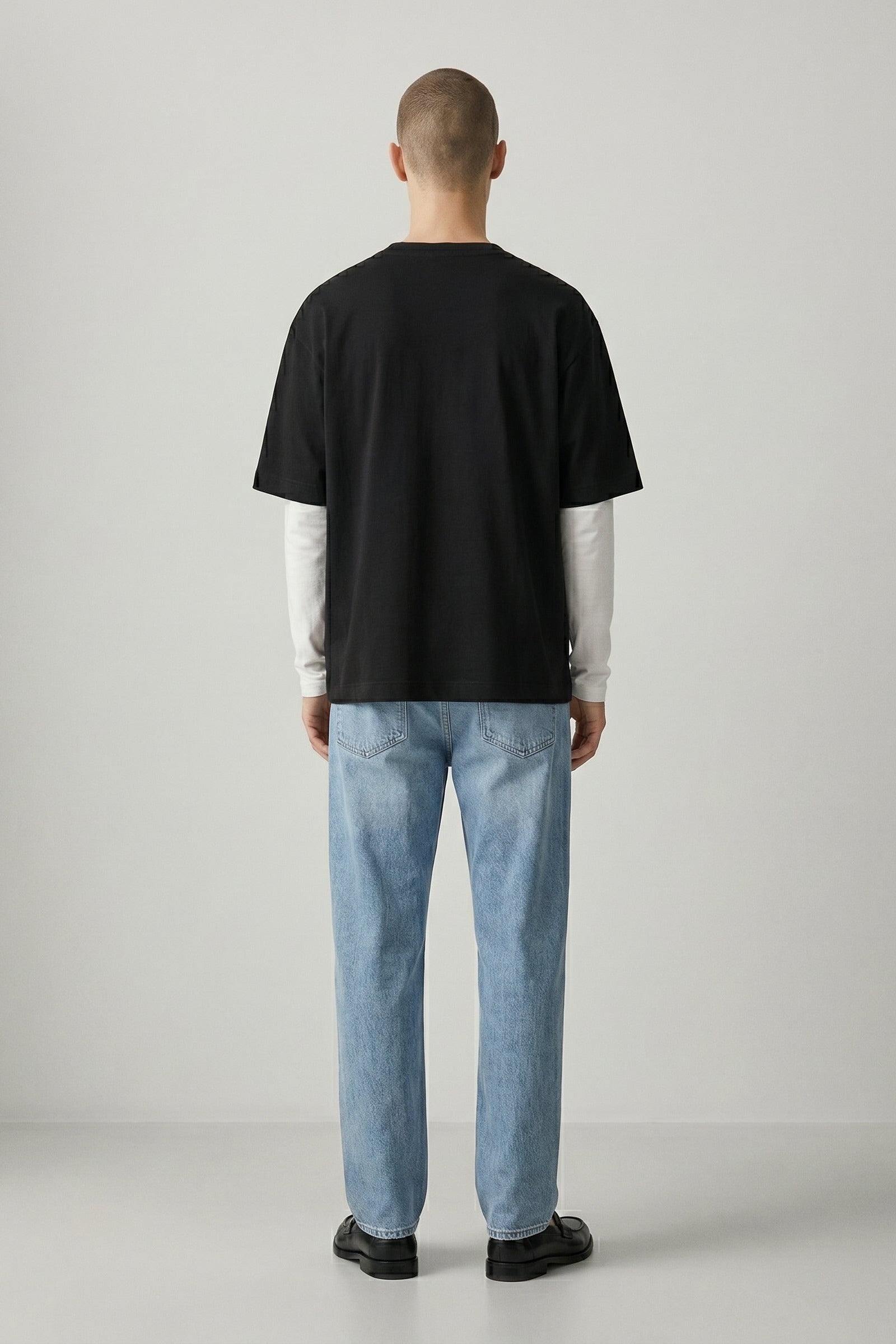 Person wearing a black t-shirt and light blue jeans standing against a plain background