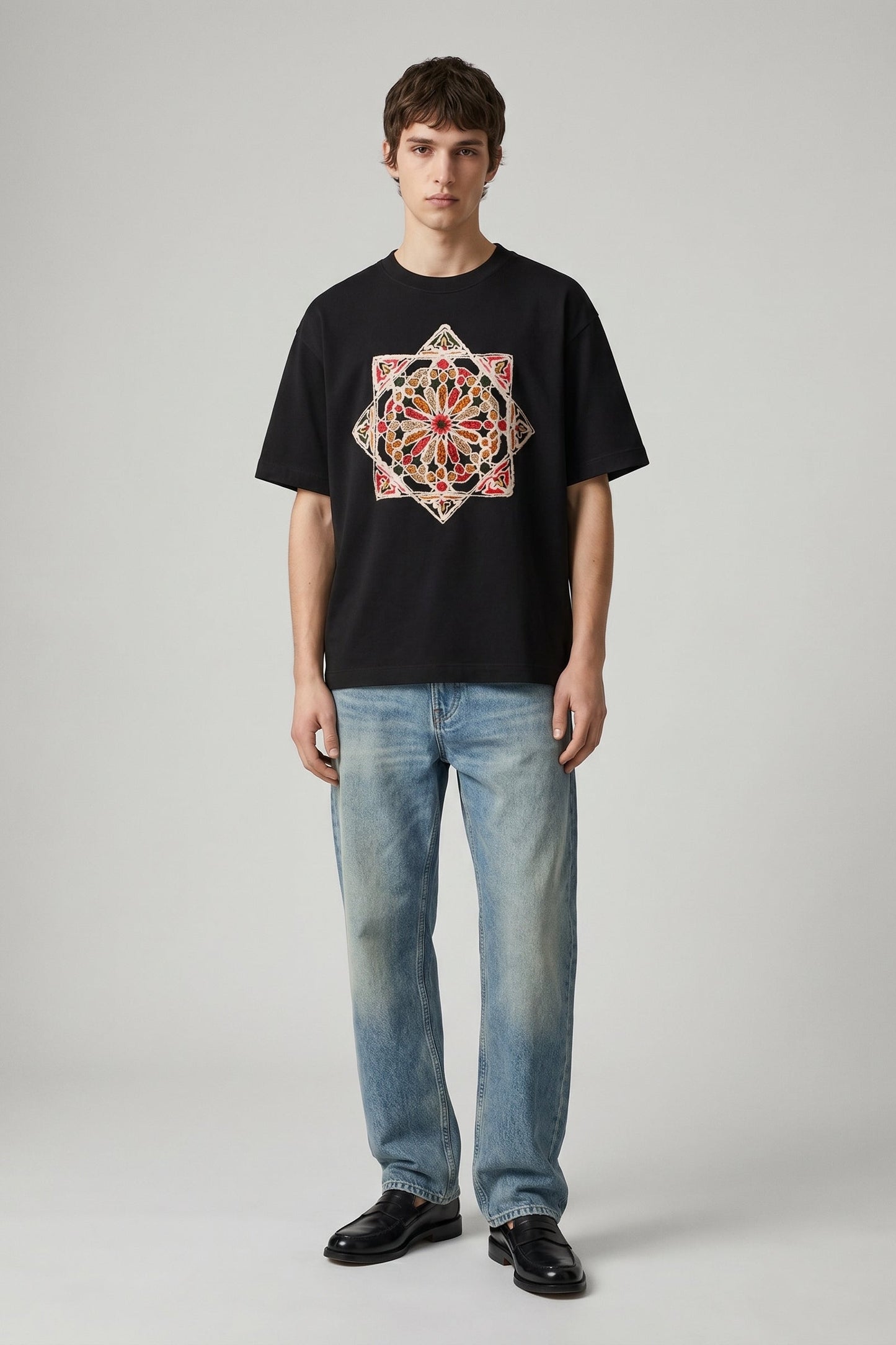 Person wearing a black t-shirt with a colorful geometric design and blue jeans on a gray background