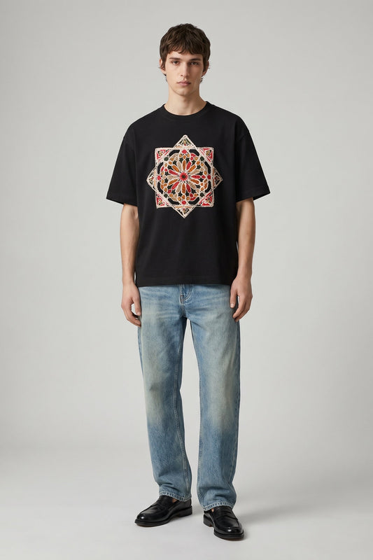Person wearing a black t-shirt with a colorful geometric design and blue jeans on a gray background