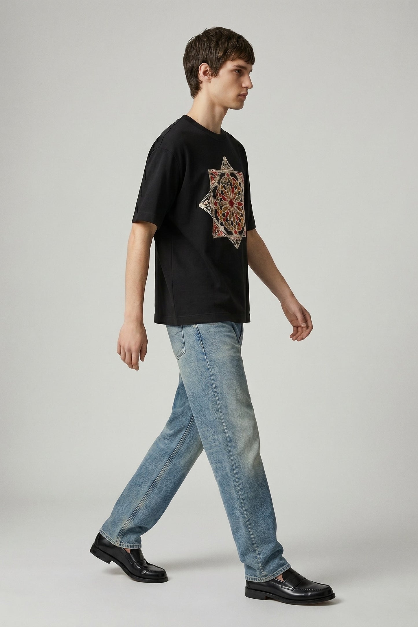 Person wearing a black t-shirt with a colorful design and light blue jeans on a gray background