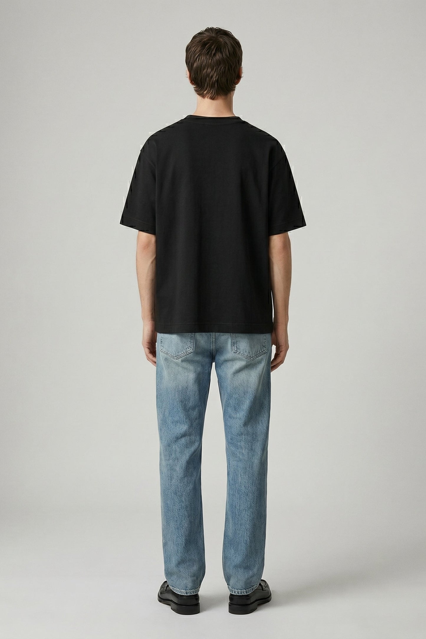 Person wearing a black t-shirt and blue jeans on a plain background