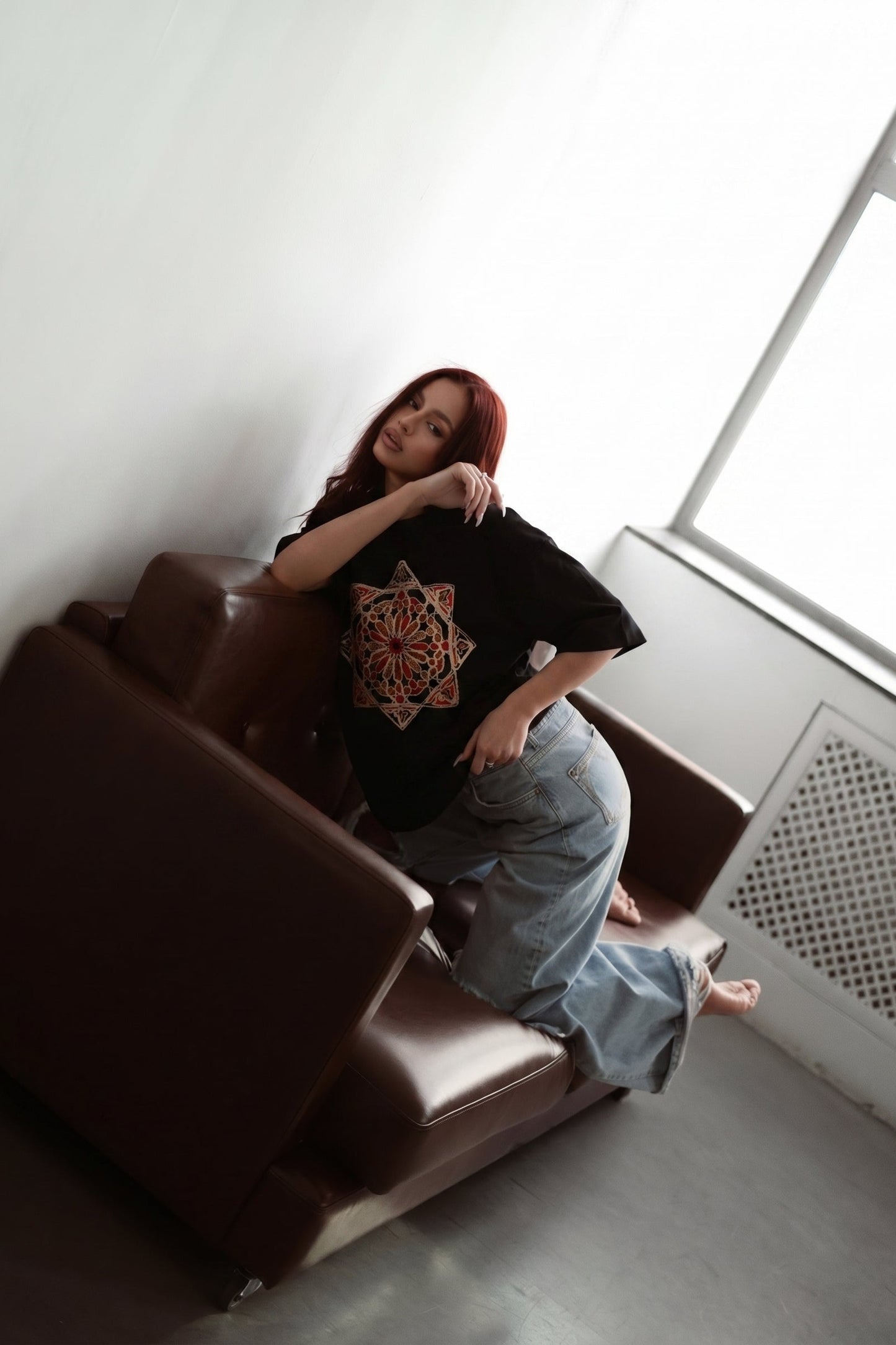 Person sitting on a brown couch in a room with a large window.