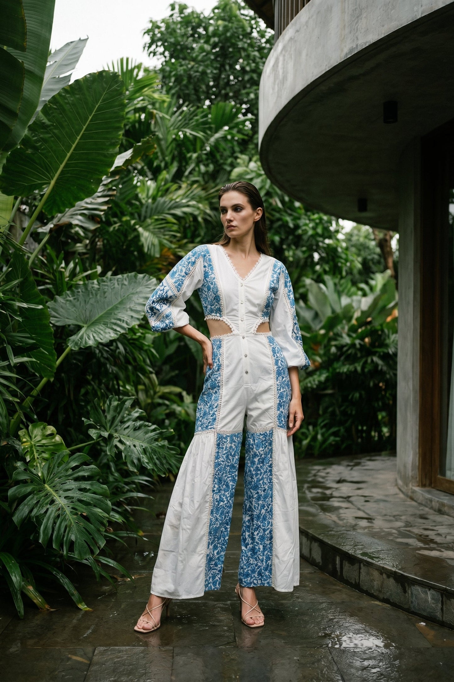 Woman in a white and blue outfit standing in a lush, tropical setting.