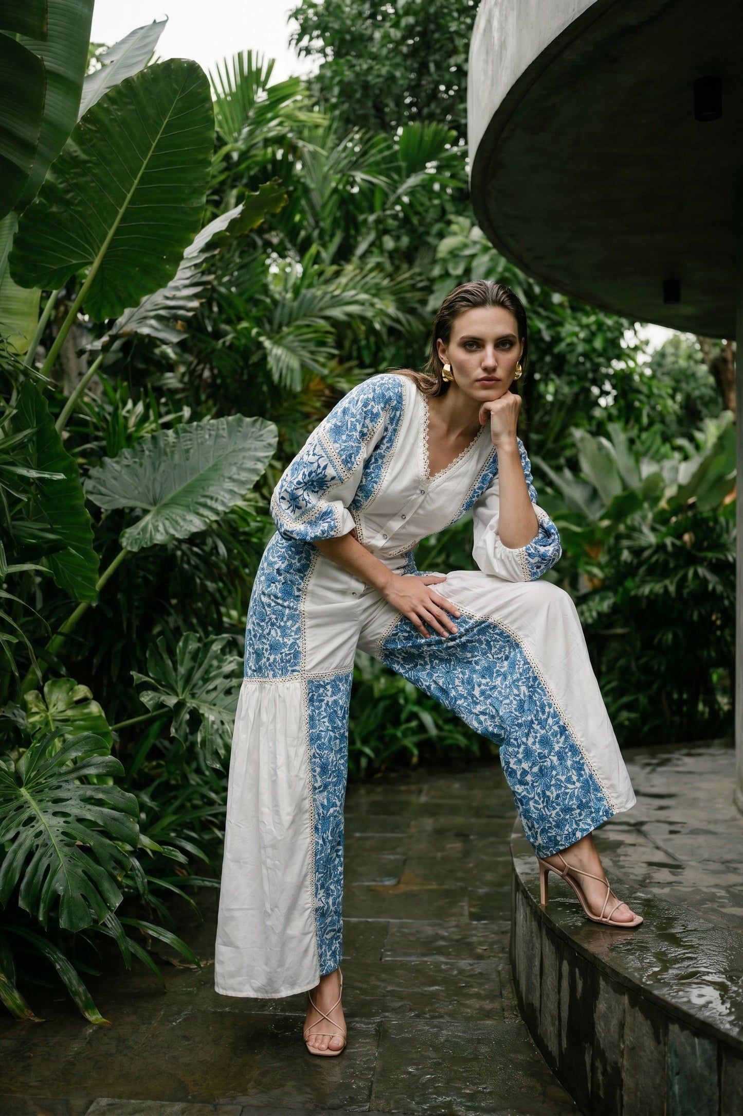 Woman in a blue and white outfit sitting on a stone ledge with lush greenery in the background
